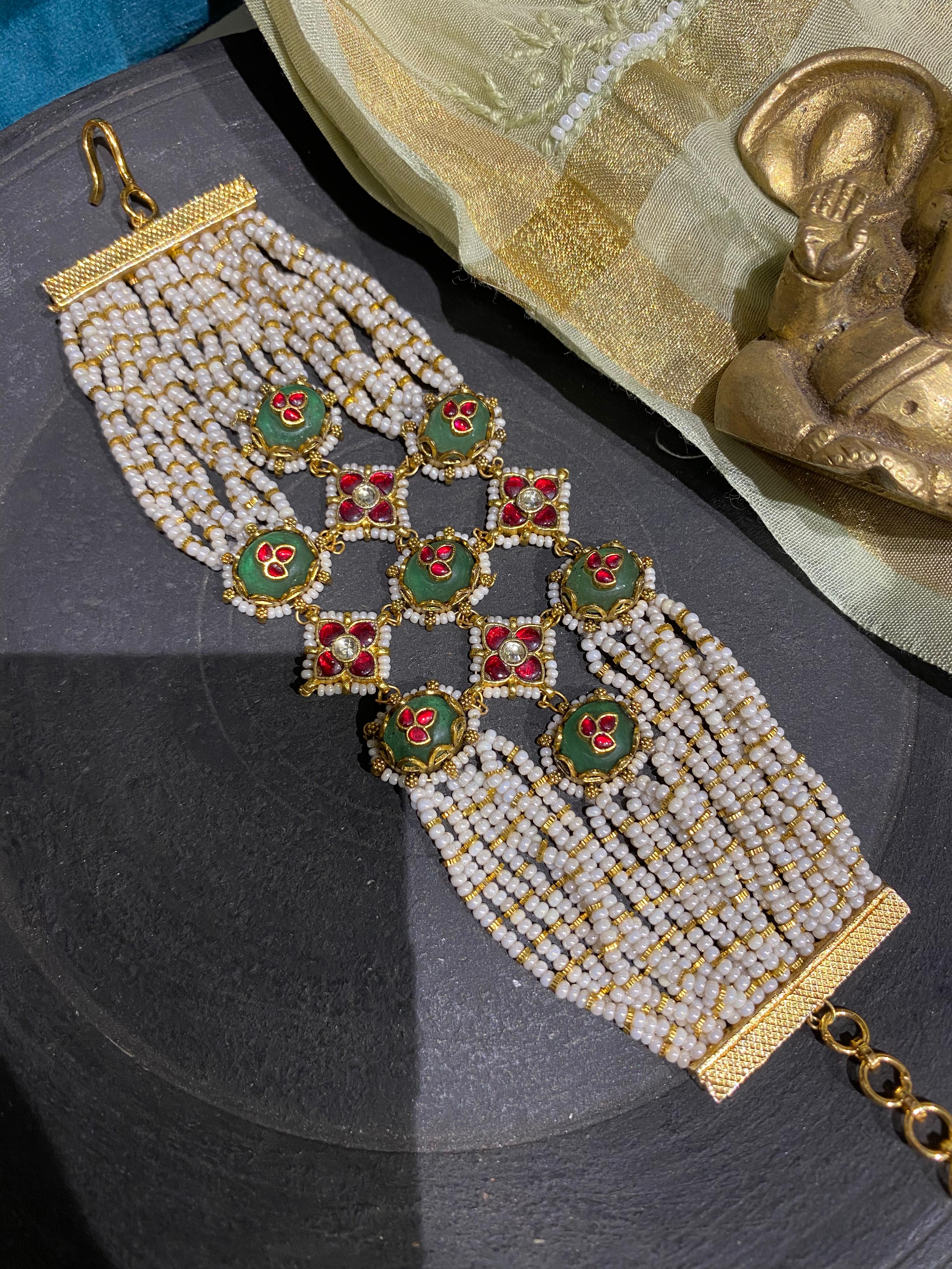 exquisite Indian ethnic wrist accessory featuring dense rows of miniature white pearls and square, gold-bordered floral elements in deep green and red.