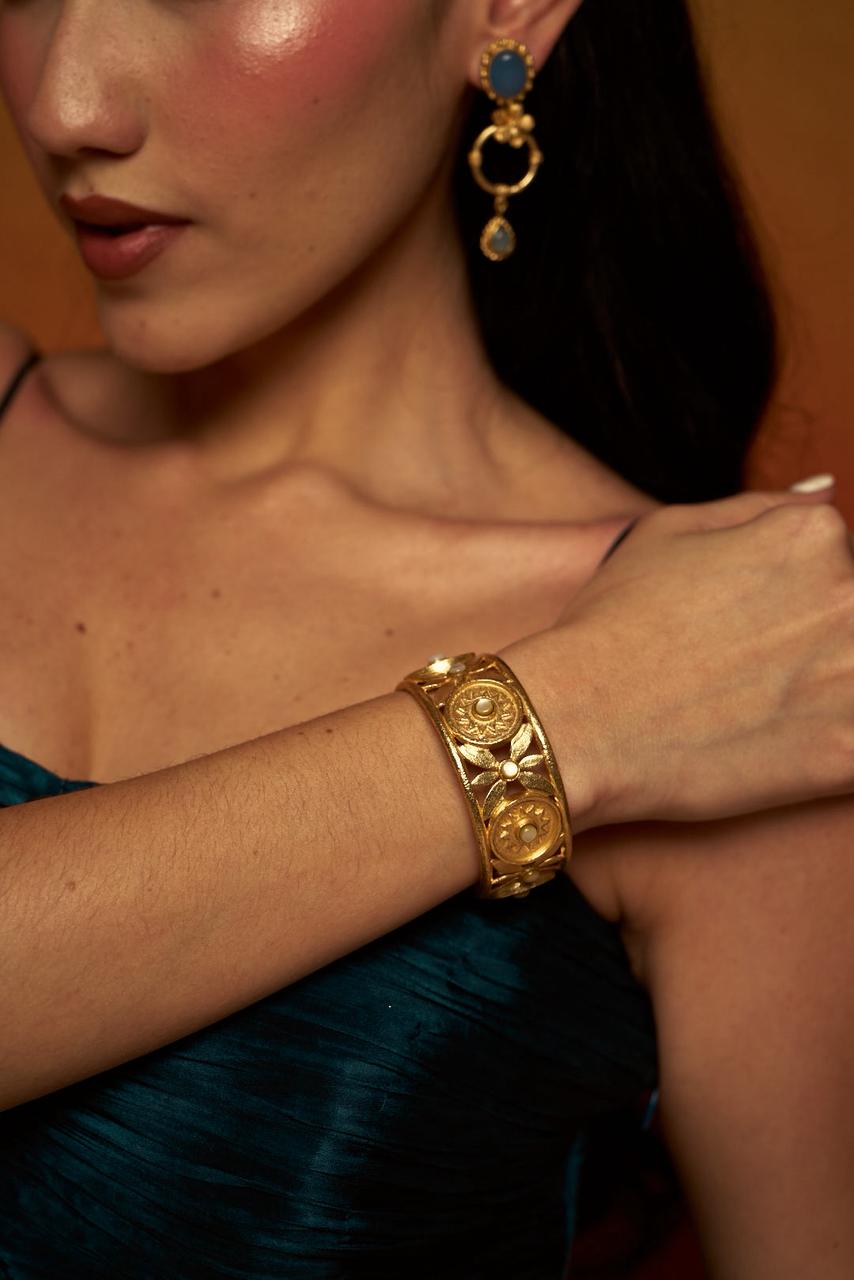 A textured gold cuff bracelet featuring intricately carved floral and sun-inspired motifs.