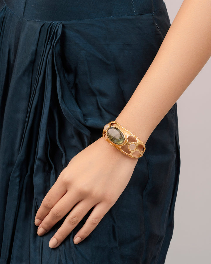 Gold bracelet with a green stone on a hand wearing a navy blue dress.