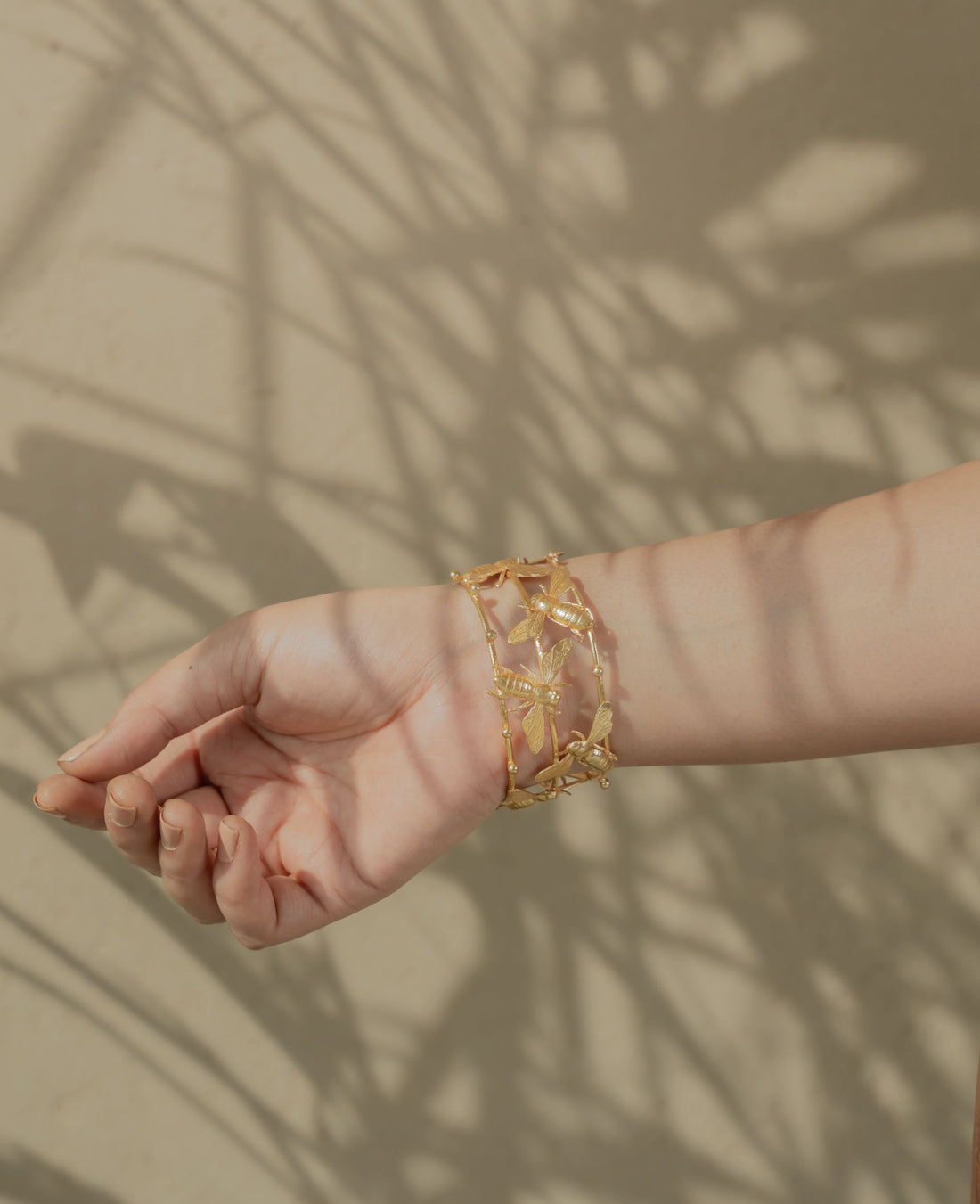 Adjustable gold-colored open cuff bracelet with bee accents resting outdoors on natural rock.