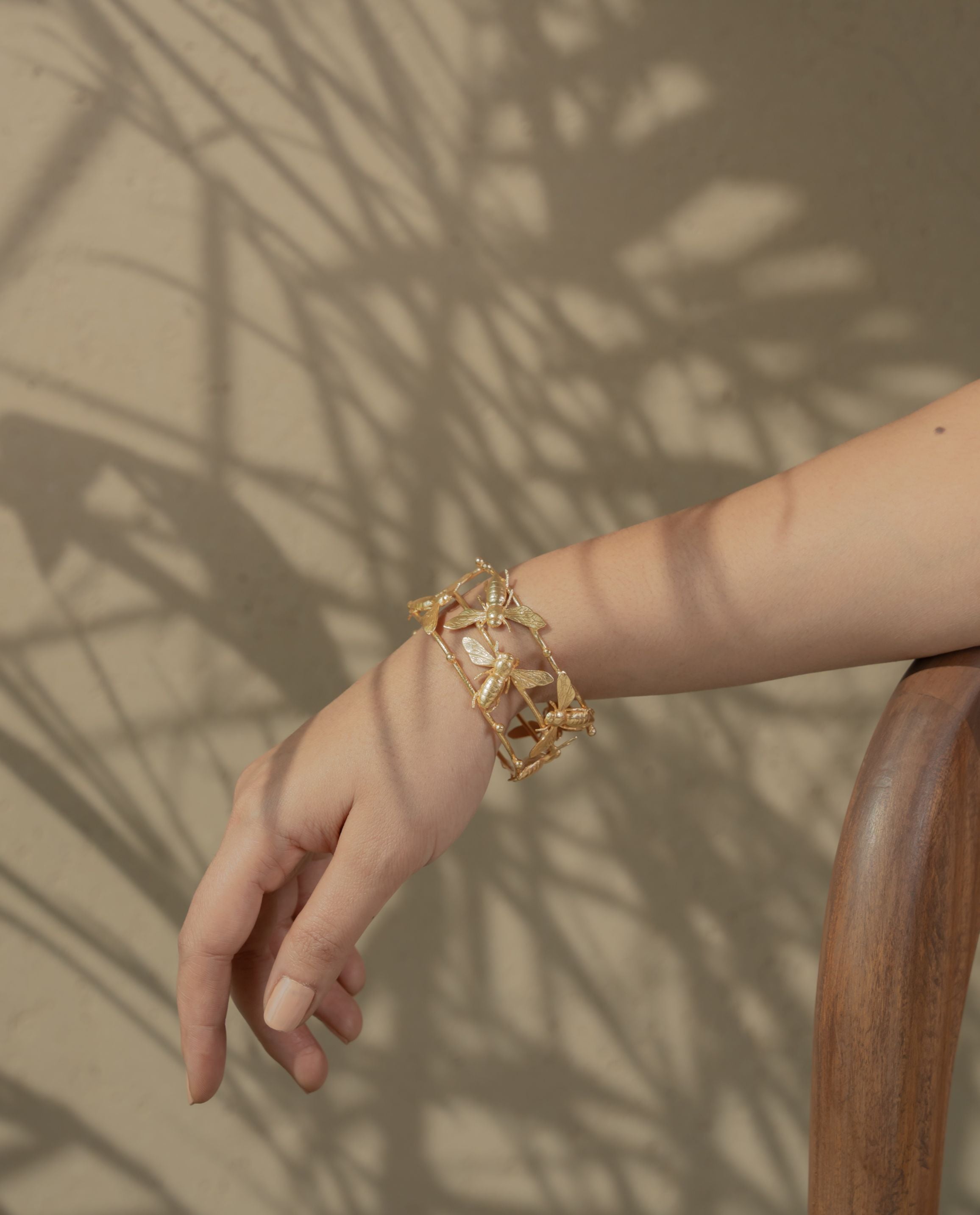 metallic gold bracelet with detailed bee designs resting on a textured rock surface.