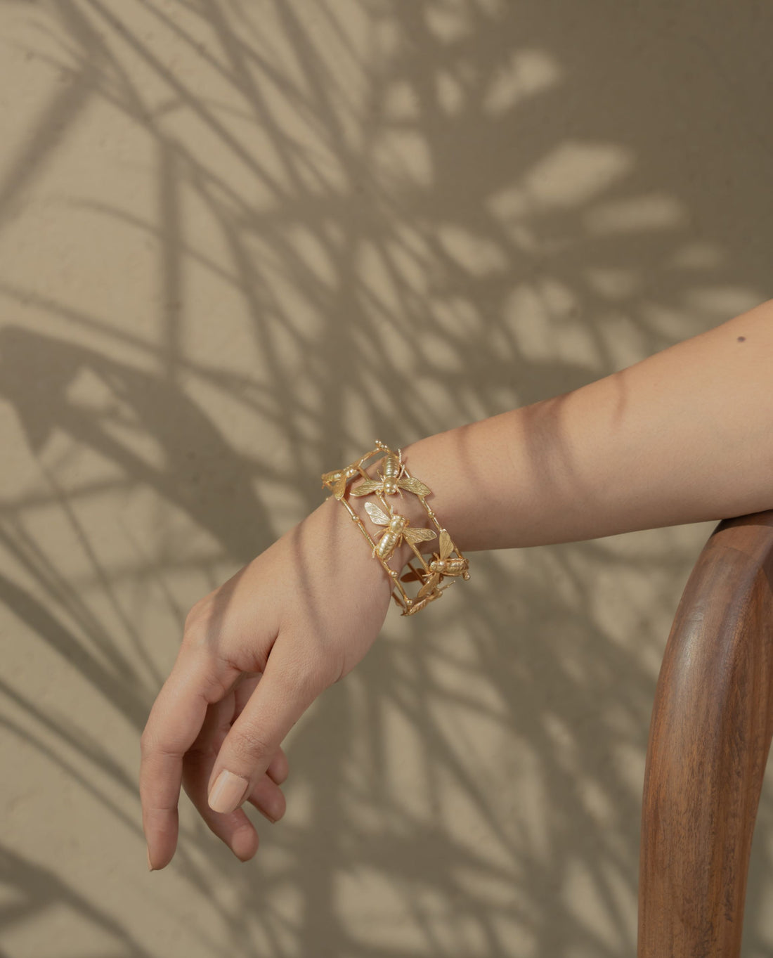 metallic gold bracelet with detailed bee designs resting on a textured rock surface.