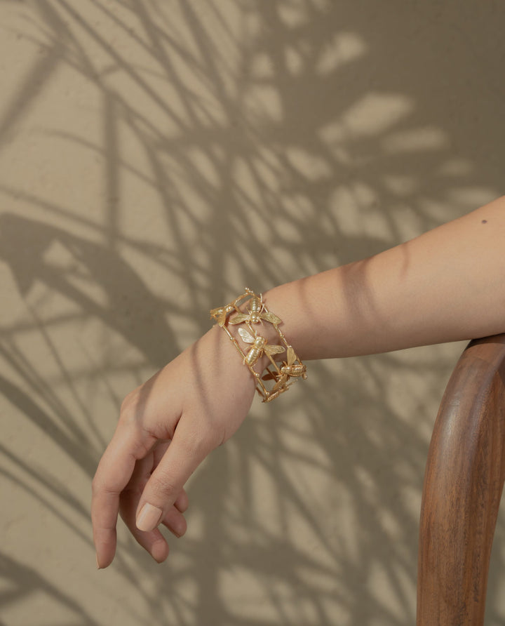 metallic gold bracelet with detailed bee designs resting on a textured rock surface.