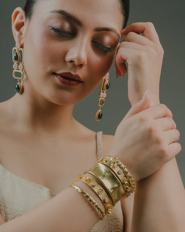 A model wearing a set of 5 chunky gold-plated stacked bracelets with floral motifs, paired with matching statement earrings.