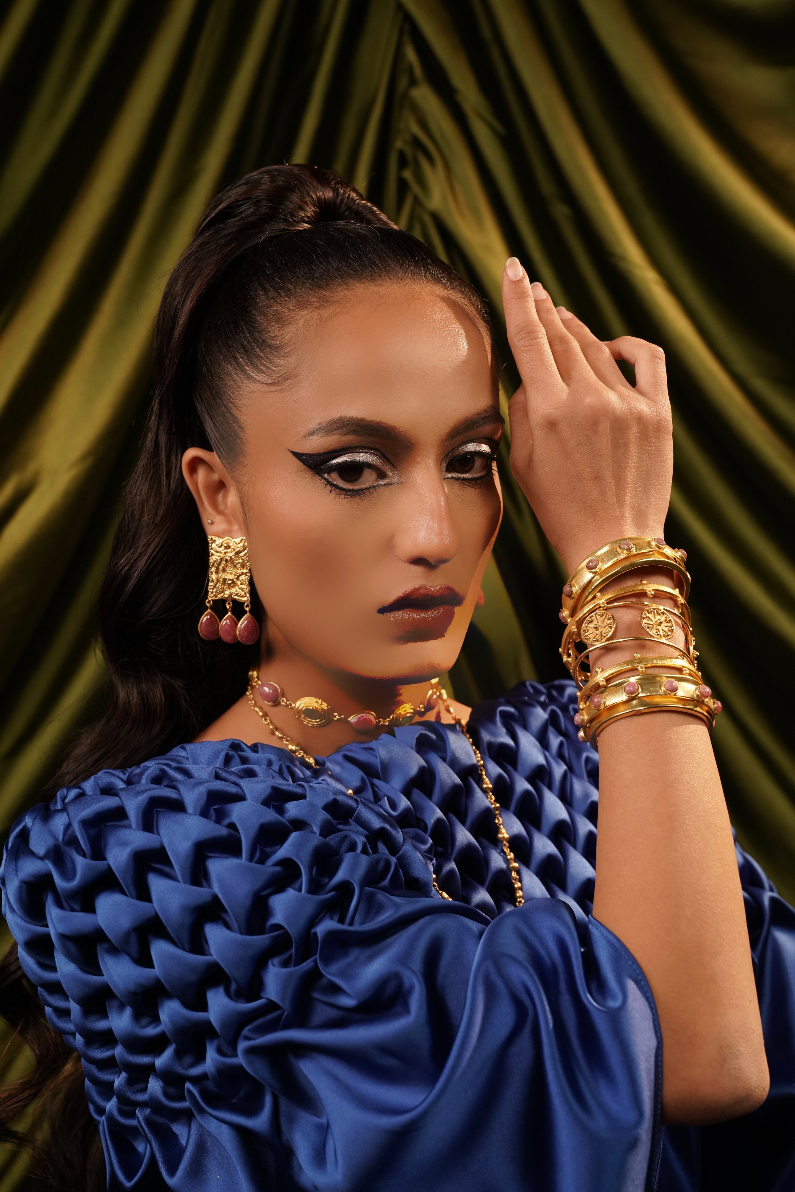 Model wearing a stack of five gold-plated bangles embellished with pink rose quartz stones and medallion motifs.