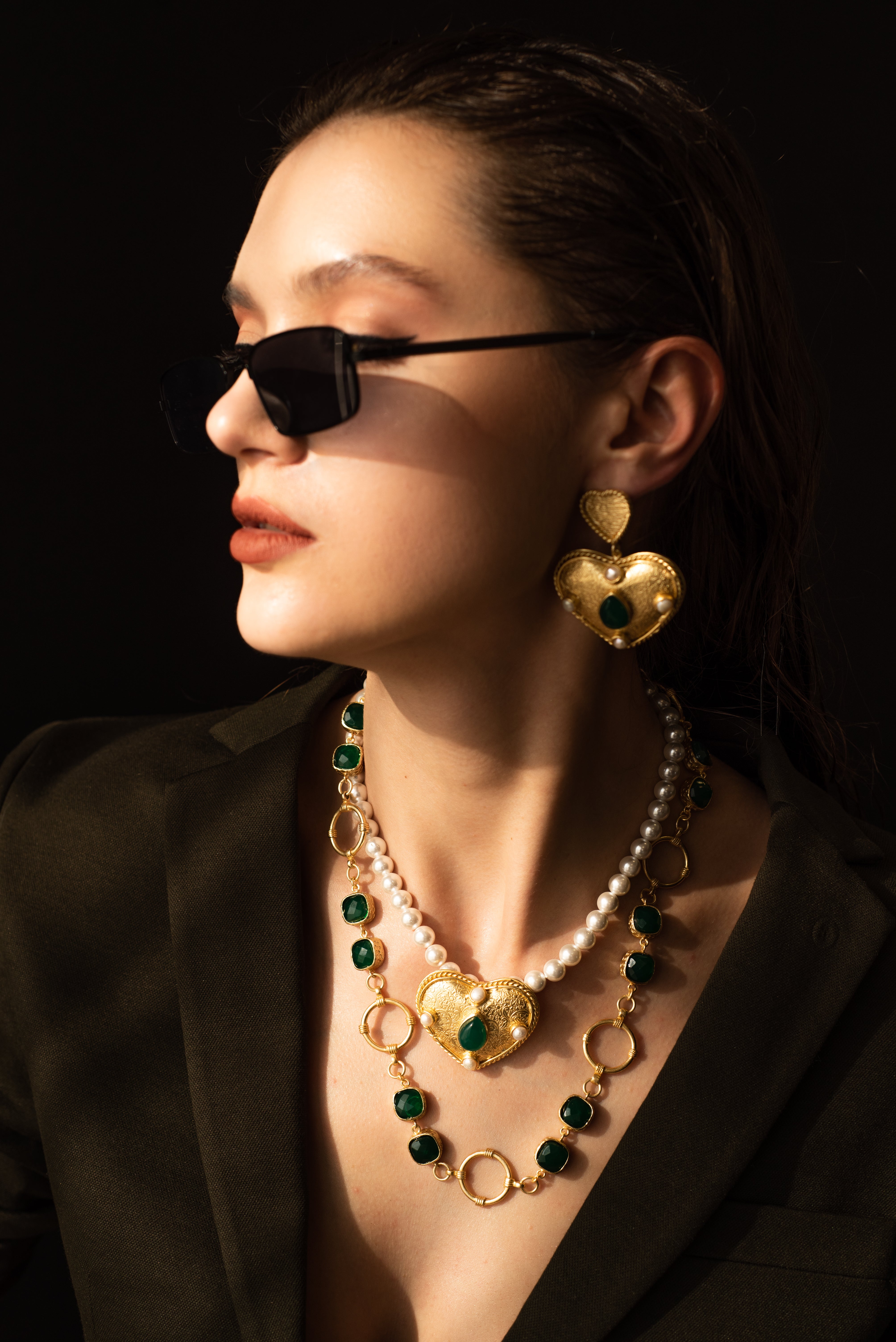 Woman posing in a patterned top wearing a gold-toned brass statement necklace featuring green crystal stones.