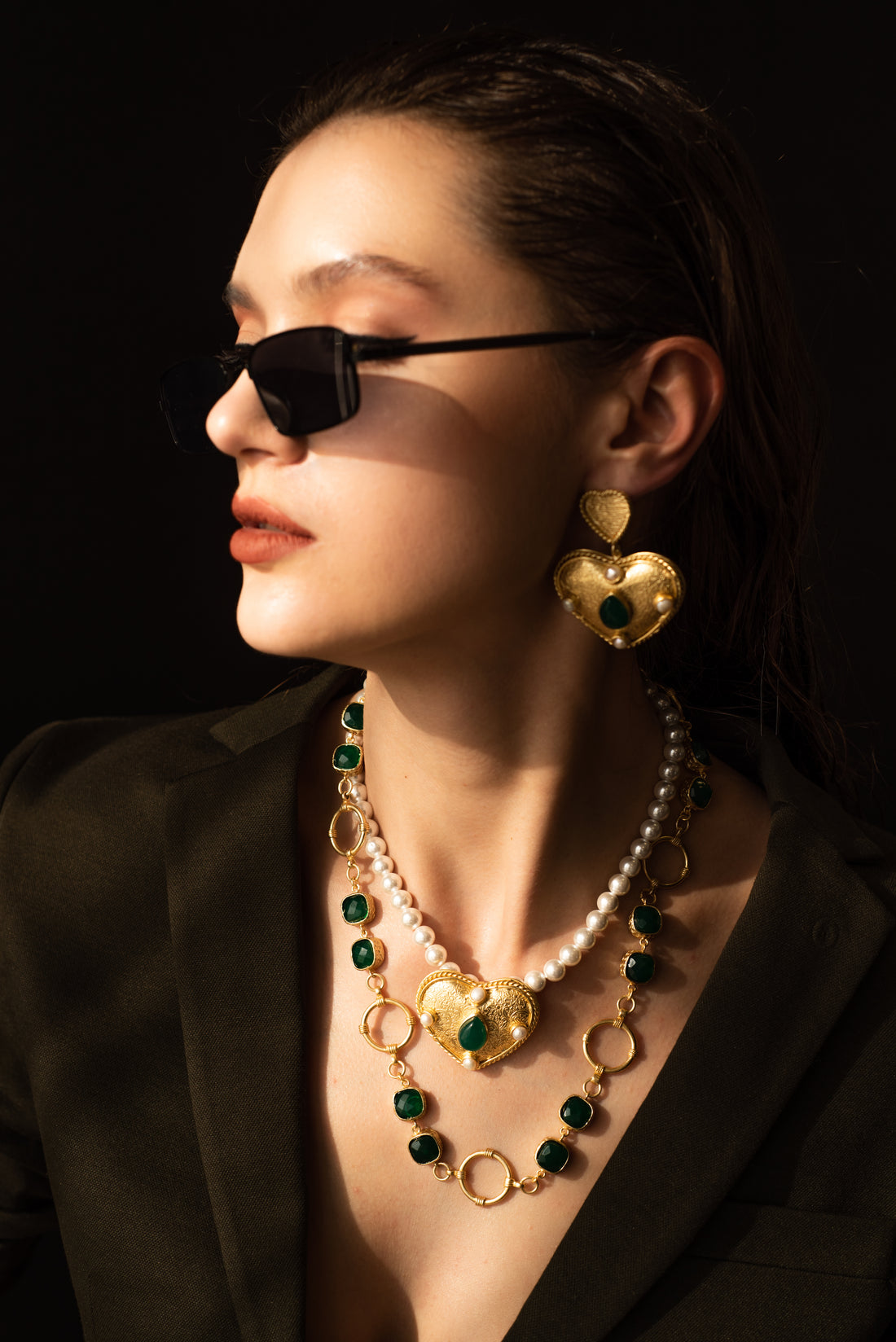 Woman posing in a patterned top wearing a gold-toned brass statement necklace featuring green crystal stones.