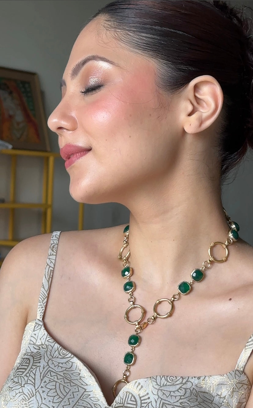 Woman wearing a gold-plated brass necklace featuring circular links and drop green stones 