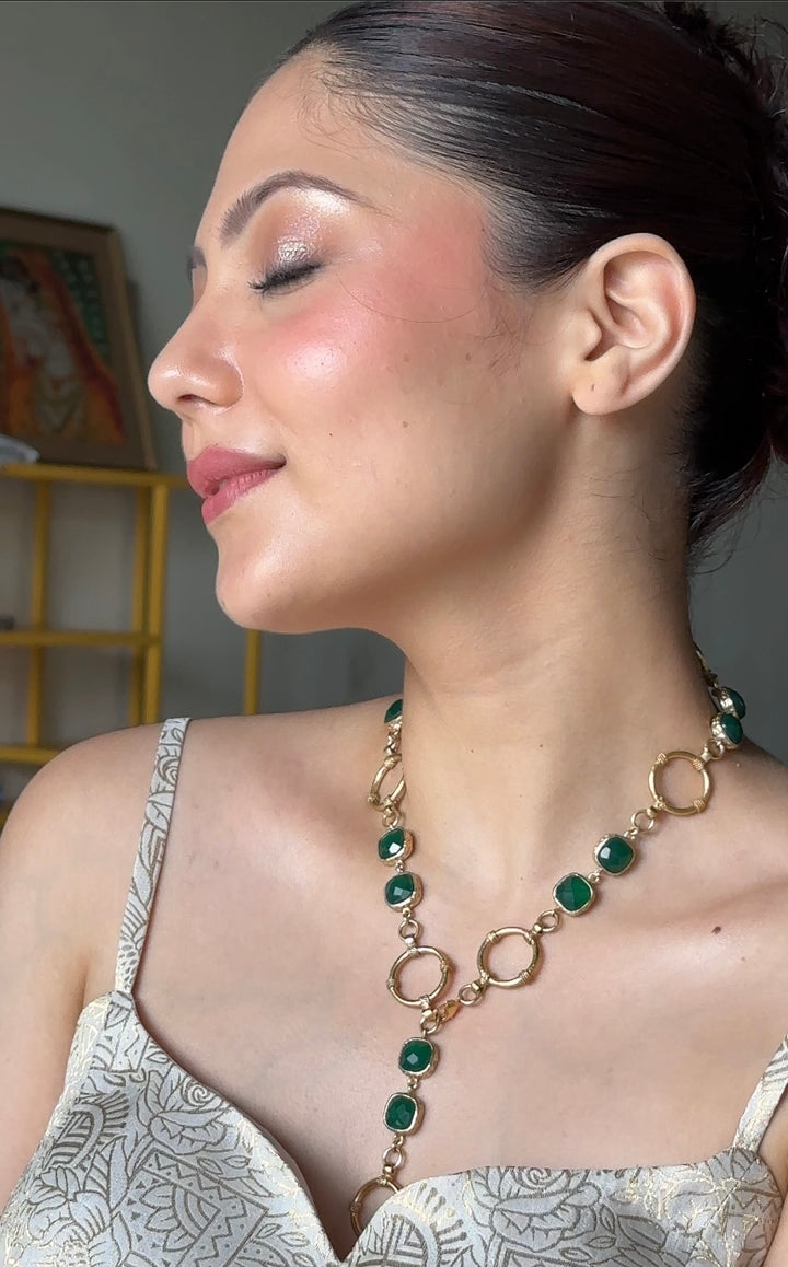 Woman wearing a gold-plated brass necklace featuring circular links and drop green stones 