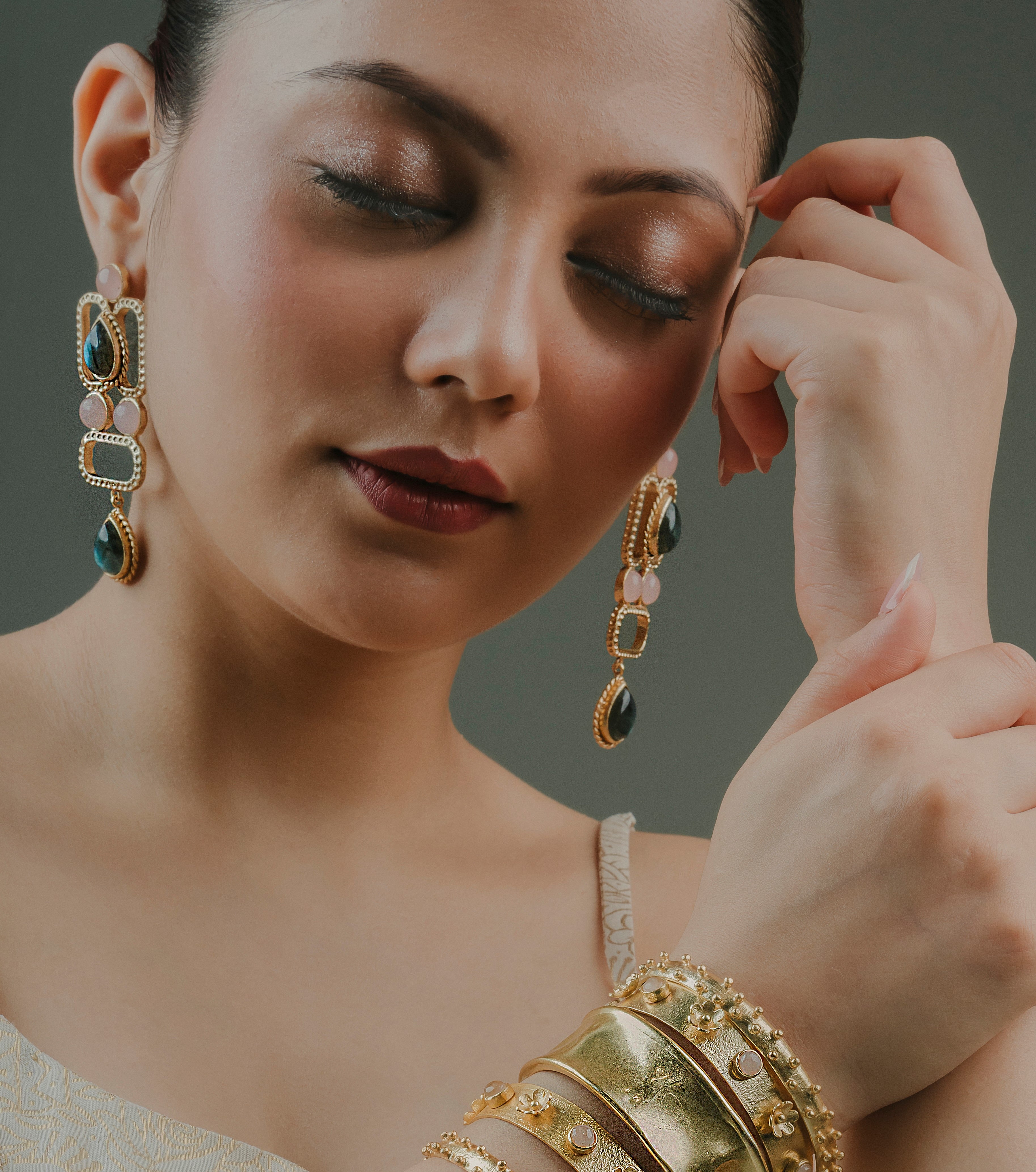 model wearing ethnic festive geometric drop earrings with gold brass finish and green stone accents.
