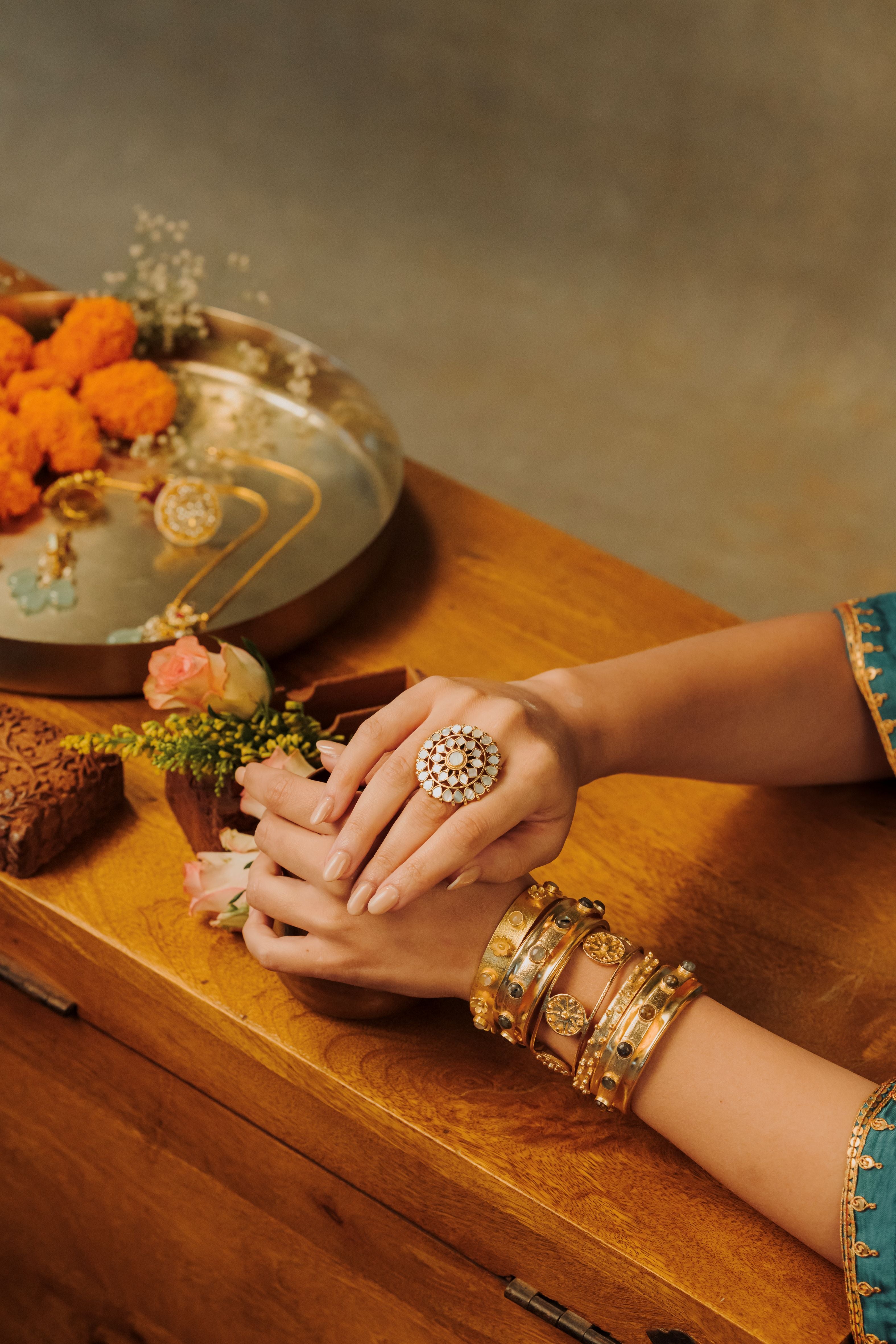 Intricate circular gold cocktail ring with mother of pearl petal clusters, styled on smooth river stones.