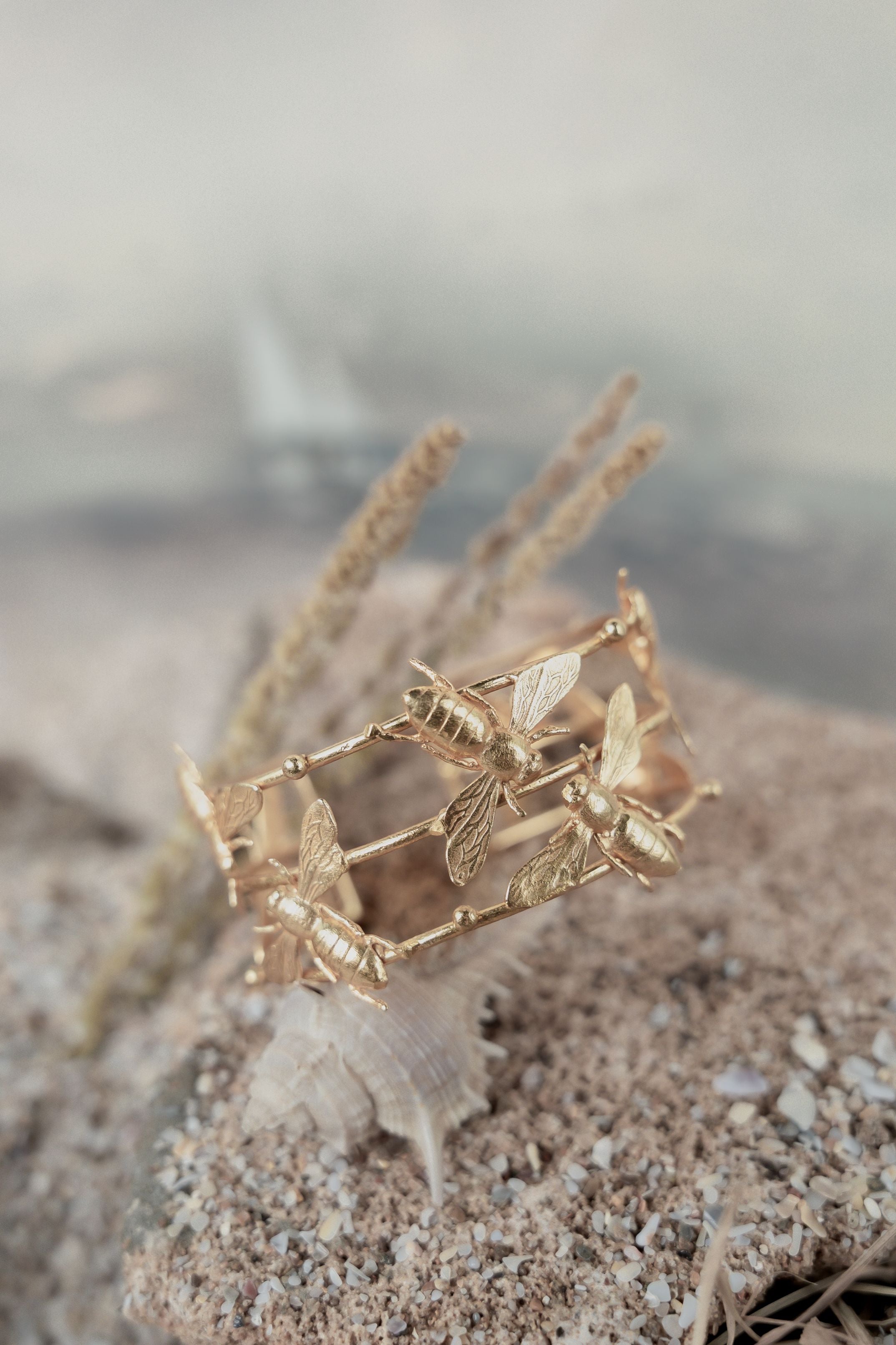 Intricately detailed gold-plated cuff bracelet featuring sculpted honeybees resting on a textured stone surface.