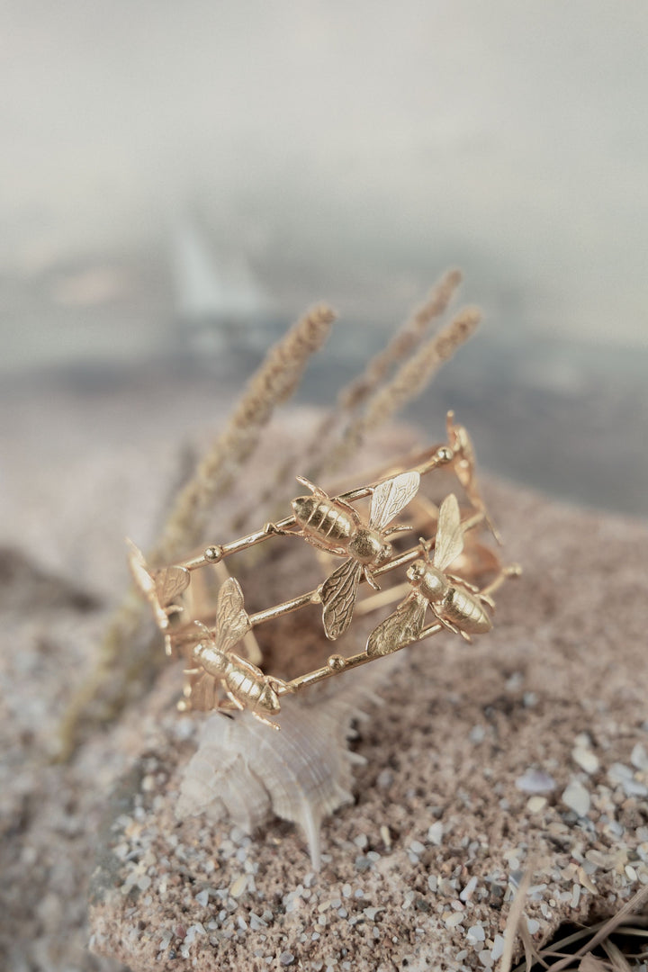 Intricately detailed gold-plated cuff bracelet featuring sculpted honeybees resting on a textured stone surface.
