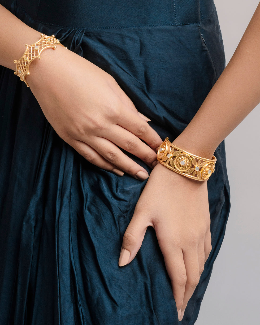 Side view of a premium openable gold-plated statement bracelet with open filigree work and central pearl-like floral details on a female wrist.