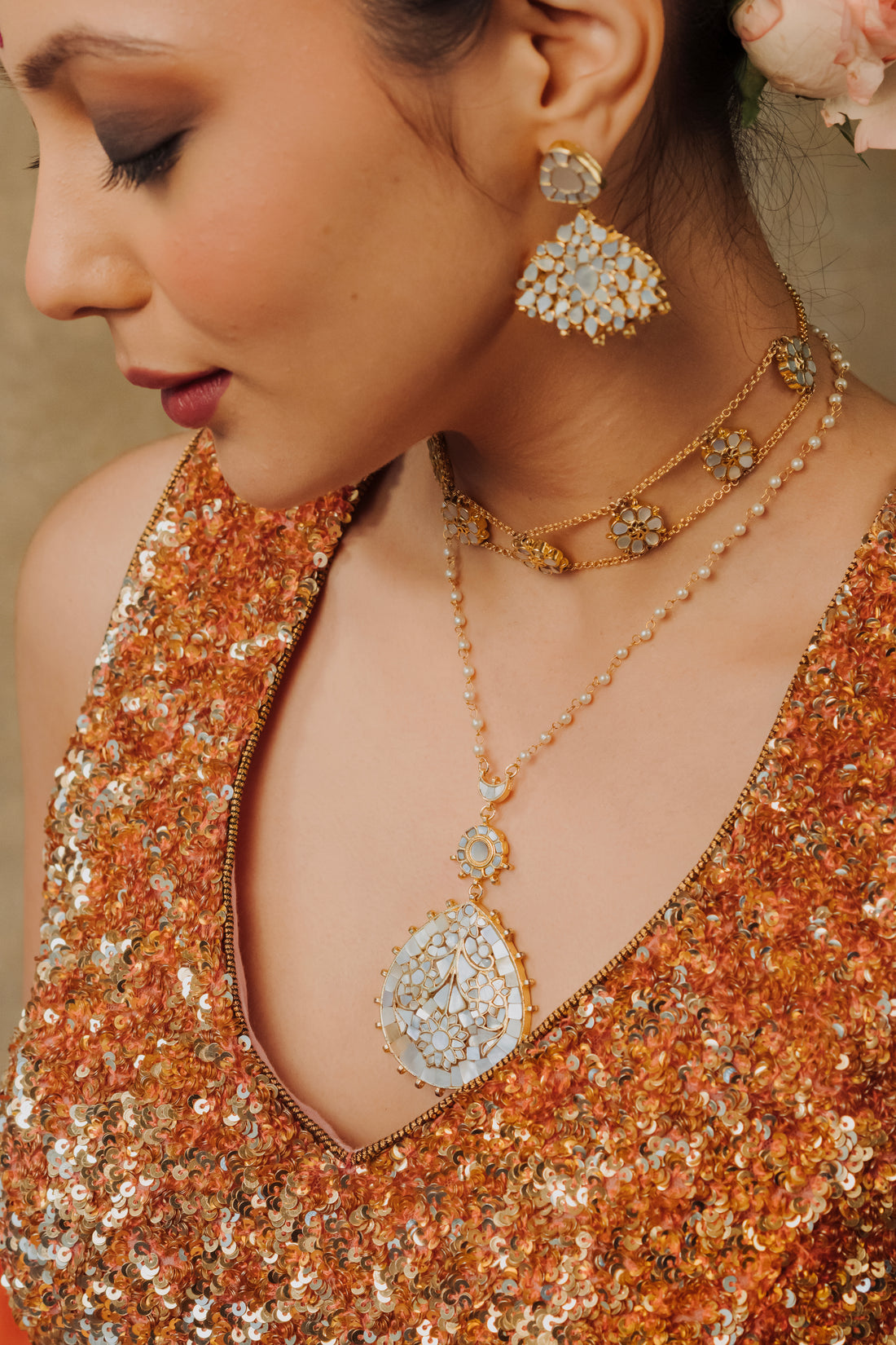 Woman wearing gold-plated mother of pearl drop necklace set with floral accents and matching statement earrings