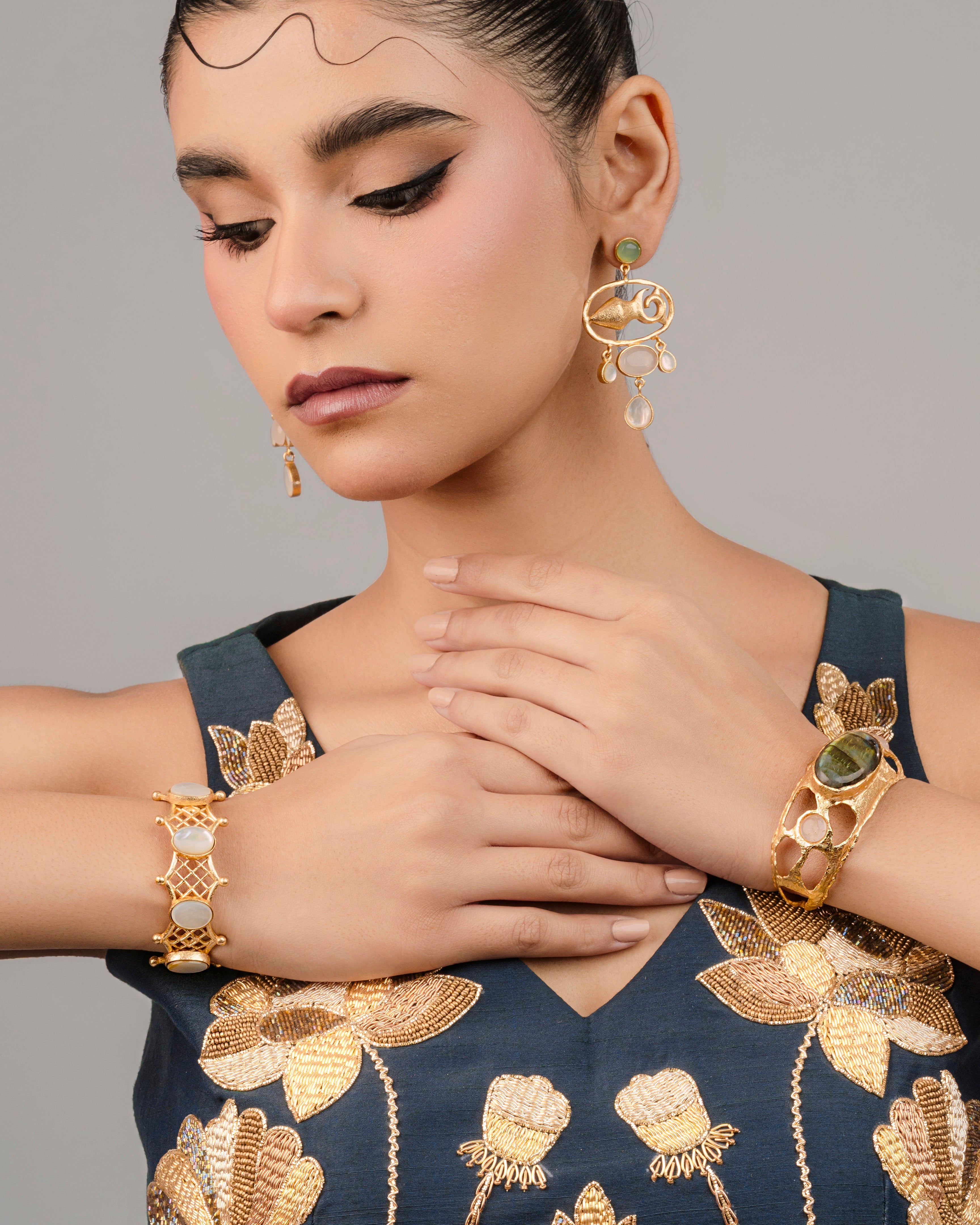 Statement jewellery piece showing a textured gold cuff bracelet with a prominent green stone styled with a navy blue dress.
