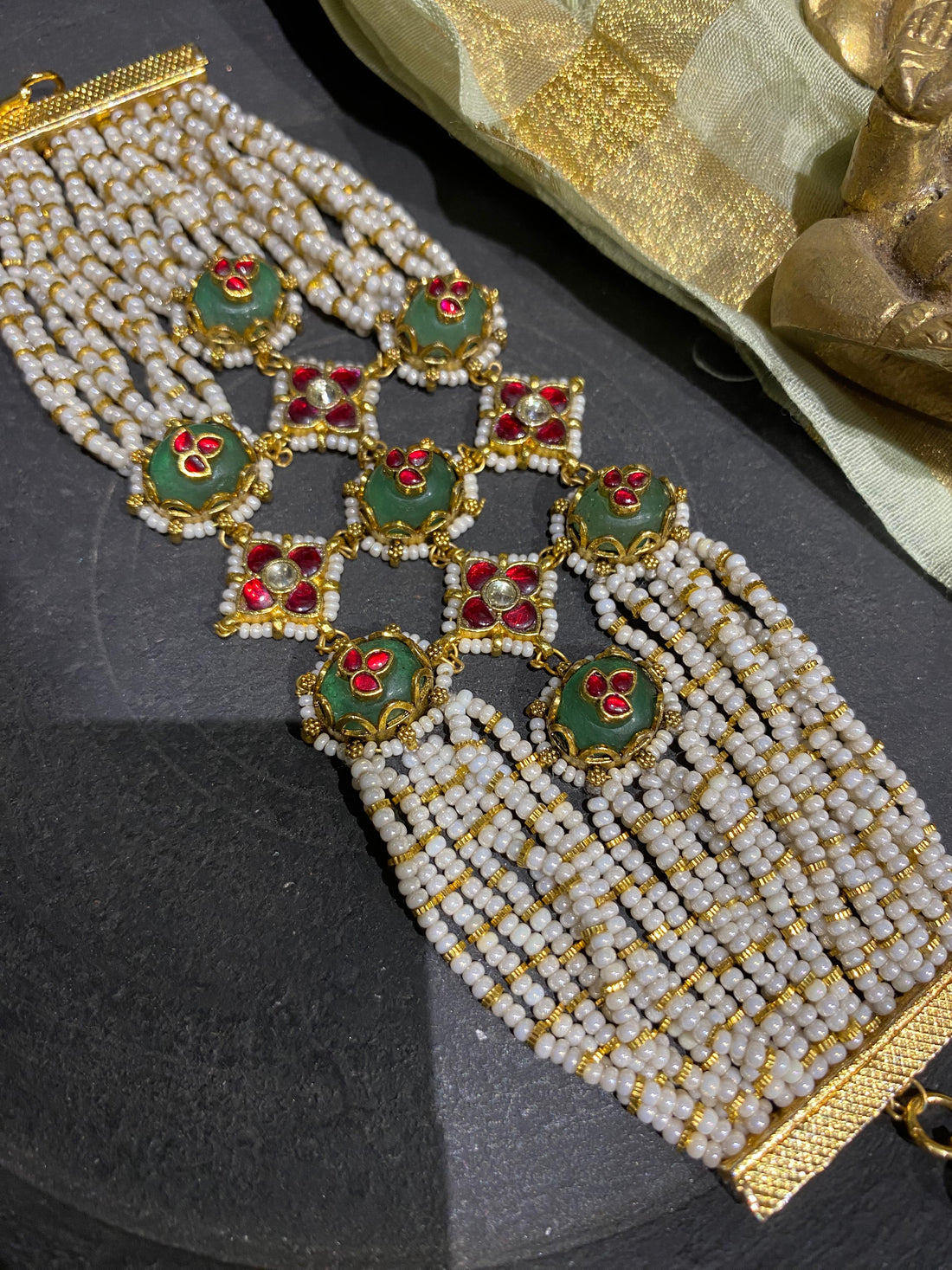 Elegant statement bracelet for festive wear showcasing meticulous hand-strung pearl layers interspersed with traditional red and green Kundan floral patterns.