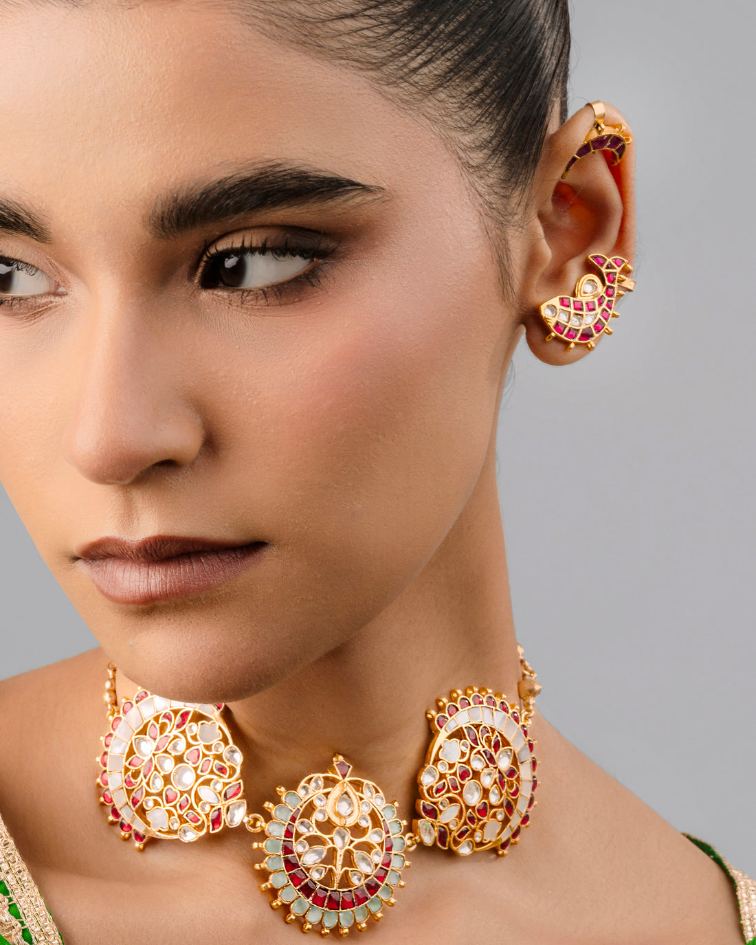 Traditional gold-plated Kundan choker necklace with red stones, floral motifs, and a pearl bead border worn by a model.