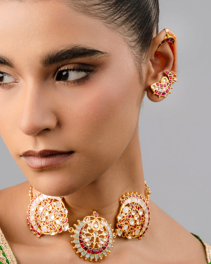 Traditional gold-plated Kundan choker necklace with red stones, floral motifs, and a pearl bead border worn by a model.