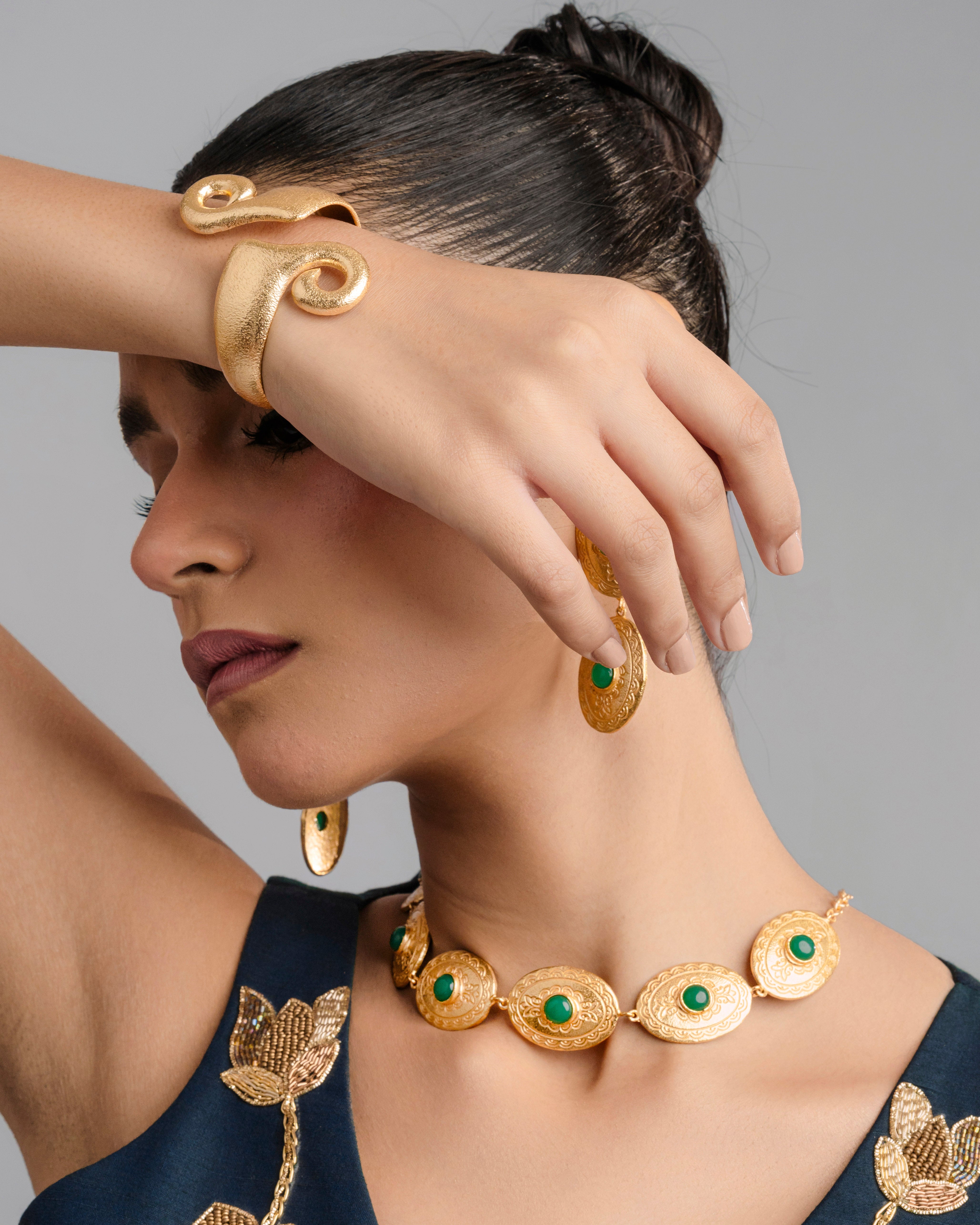 Modern adjustable gold arm cuff with a distinct wave-like spiral structure, beautifully contrasting against a dark navy fabric backdrop.