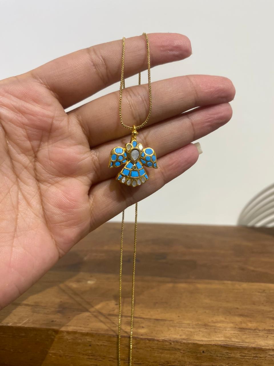 A gold-toned traditional eagle pendant featuring intricate blue turquoise mosaic wings and a pearlescent centrepiece.