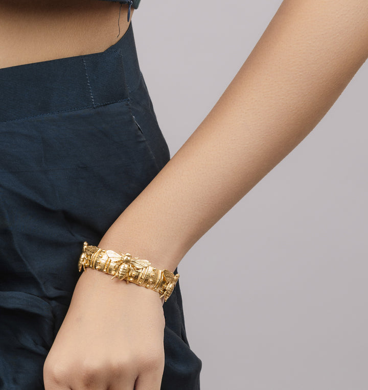 A woman wearing a chunky gold-plated cuff bracelet featuring an intricate, sculptural honey bee motif around the wrist.