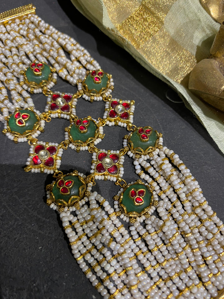 A heavy festive jewellery piece for women displaying a stunning contrast of rich green enamel, ruby-red centre stones, and multiple delicate strands of shimmering white pearls.