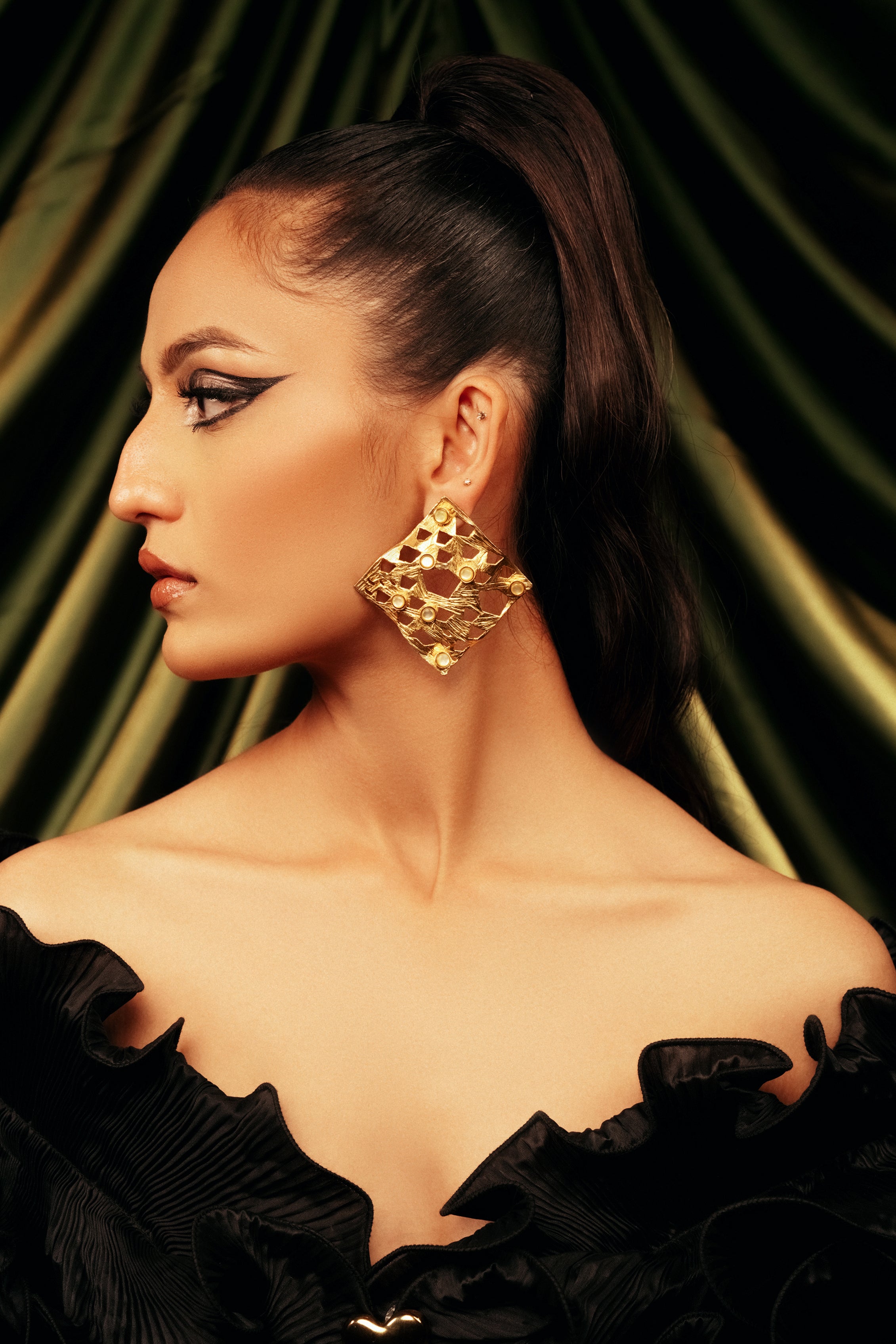 Woman wearing oversized 18k gold-plated lattice statement drop earrings with an intricate cutout design, paired with an off-shoulder black dress.
