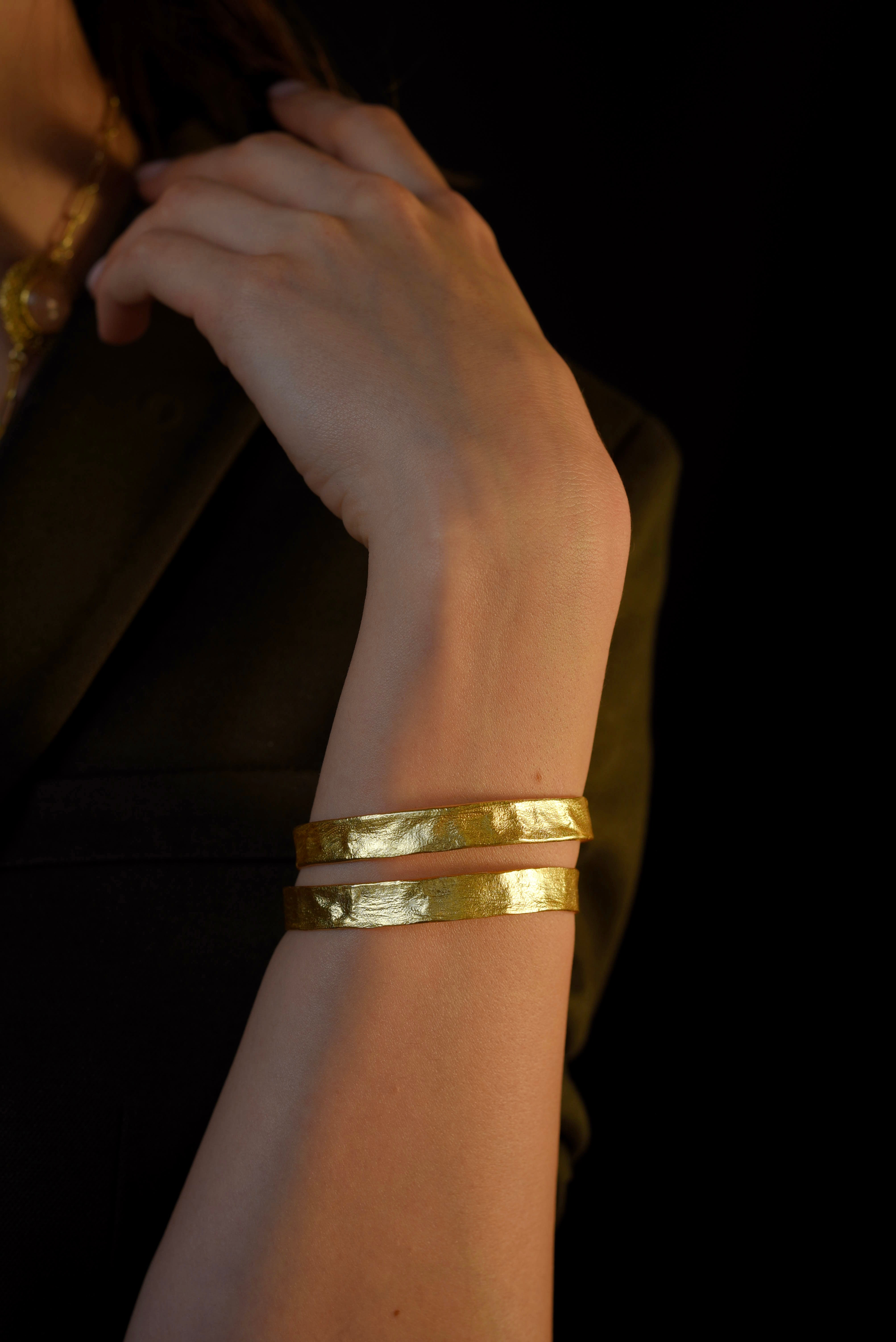 Model wearing a thick, textured gold-plated adjustable cuff bangle bracelet