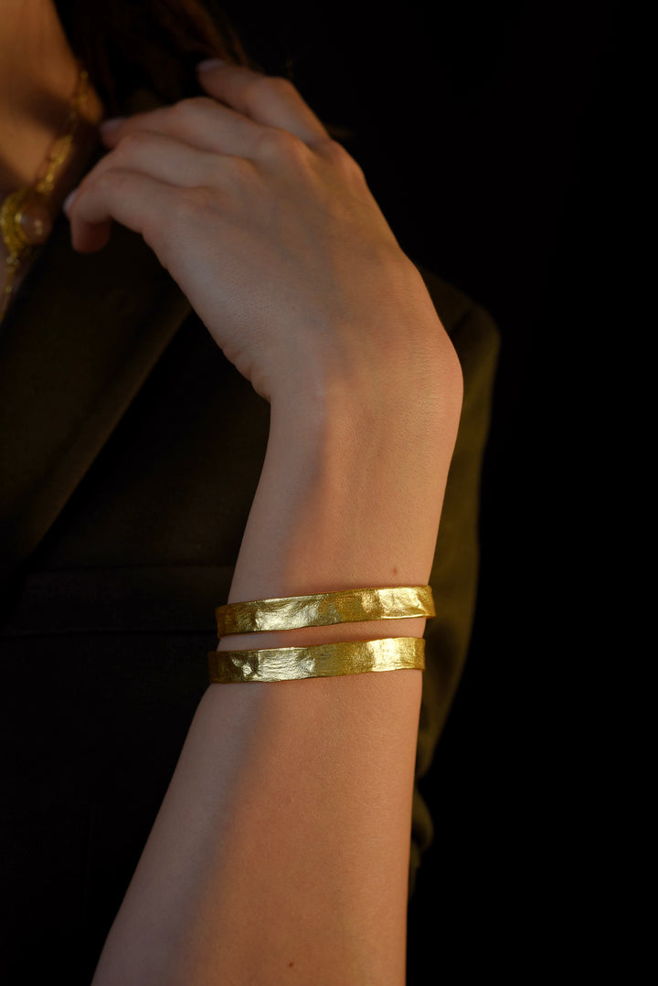 Model wearing a thick, textured gold-plated adjustable cuff bangle bracelet