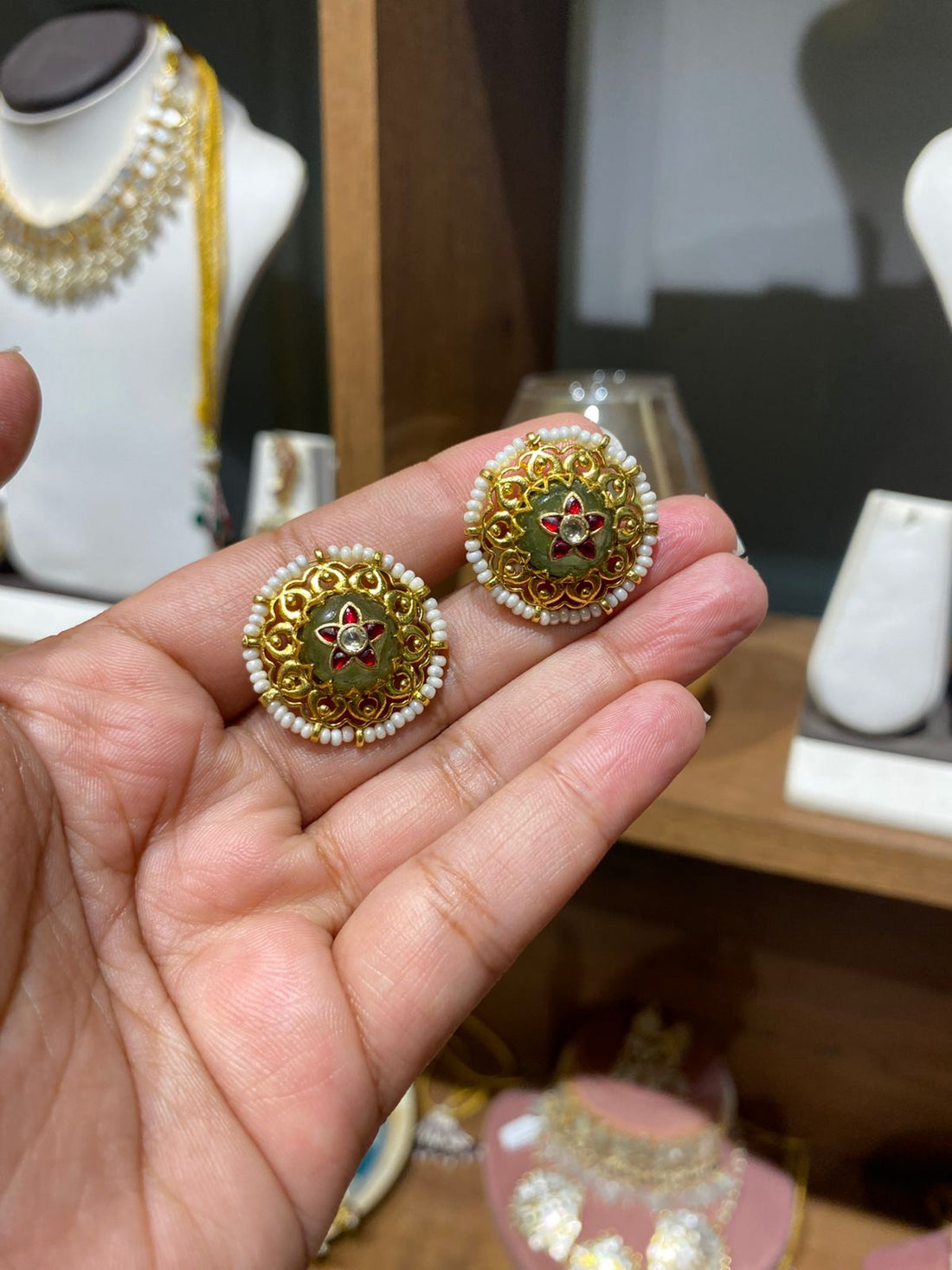 Round gold-toned alloy stud earrings with a red floral center, green base, and a delicate white pearl border.