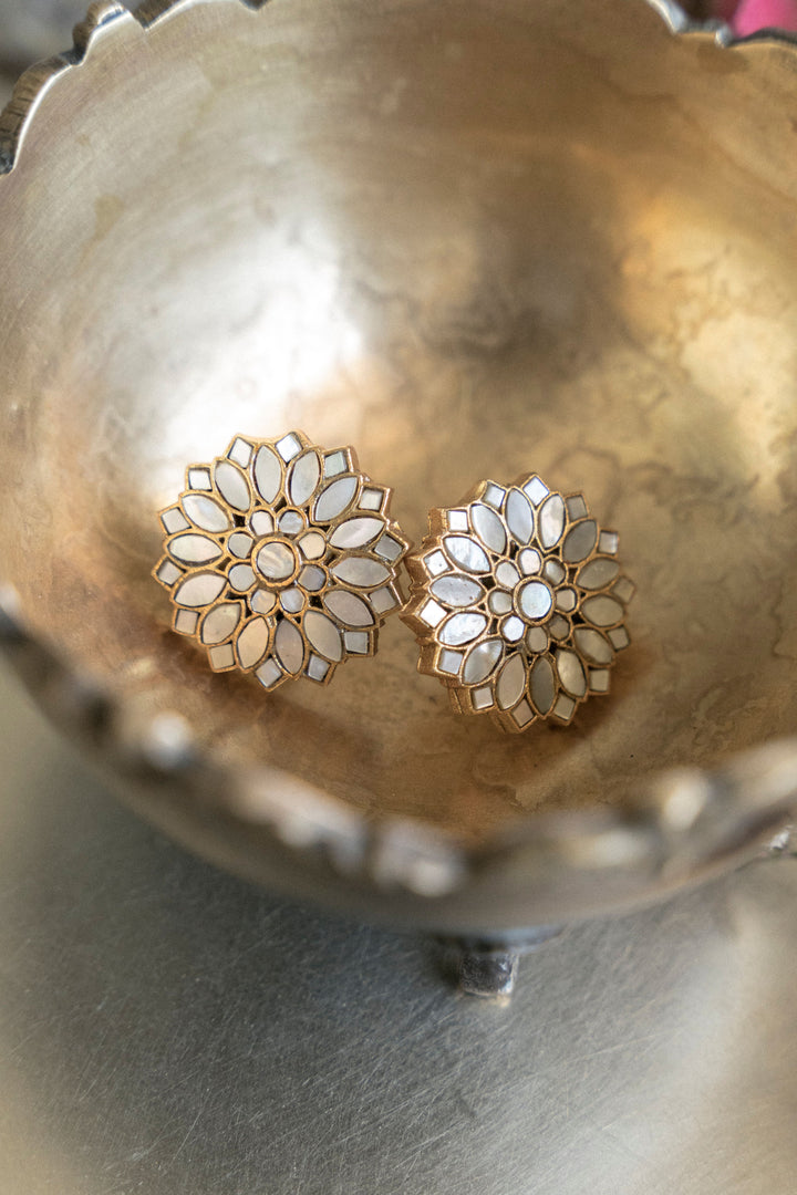 Pair of gold floral mother of pearl stud earrings resting in a metallic bowl