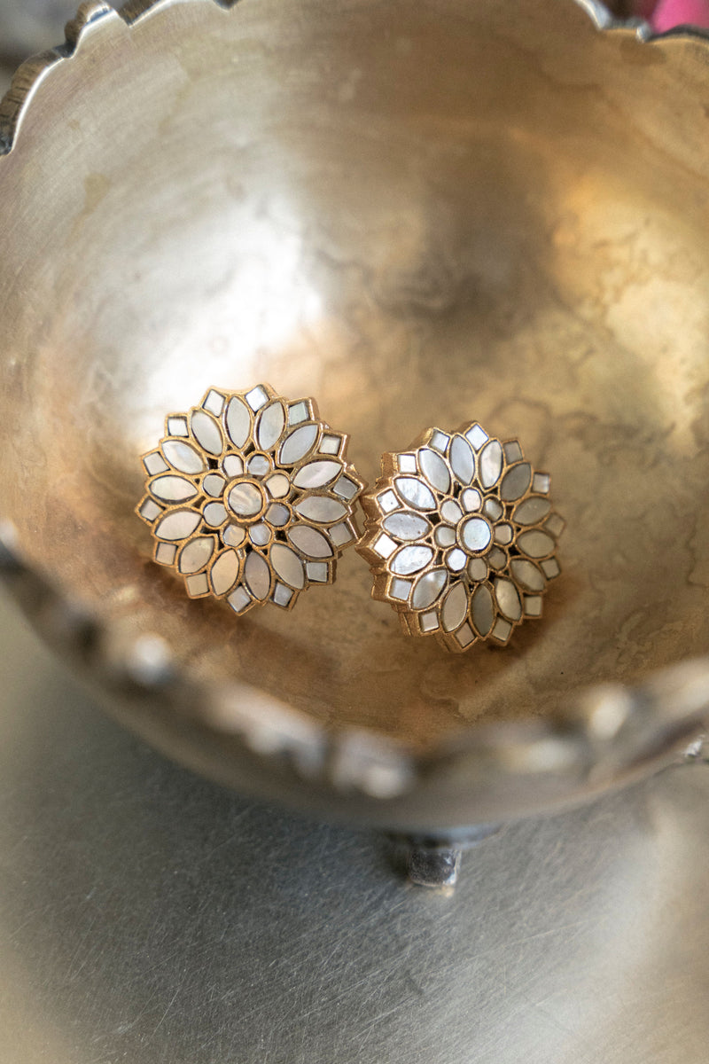 Pair of gold floral mother of pearl stud earrings resting in a metallic bowl