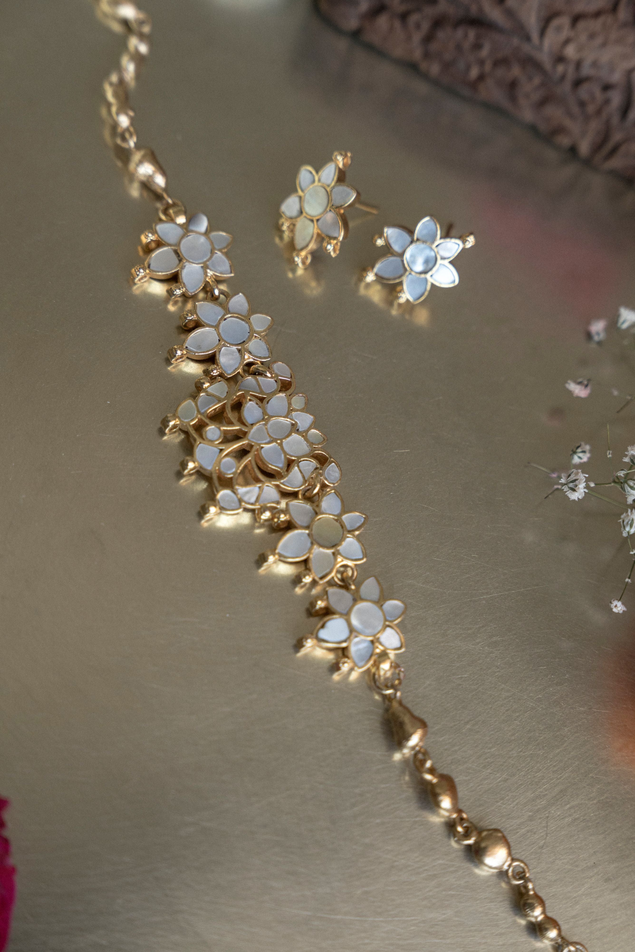 Gold-plated mother of pearl floral choker necklace with matching flower stud earrings set on a surface.