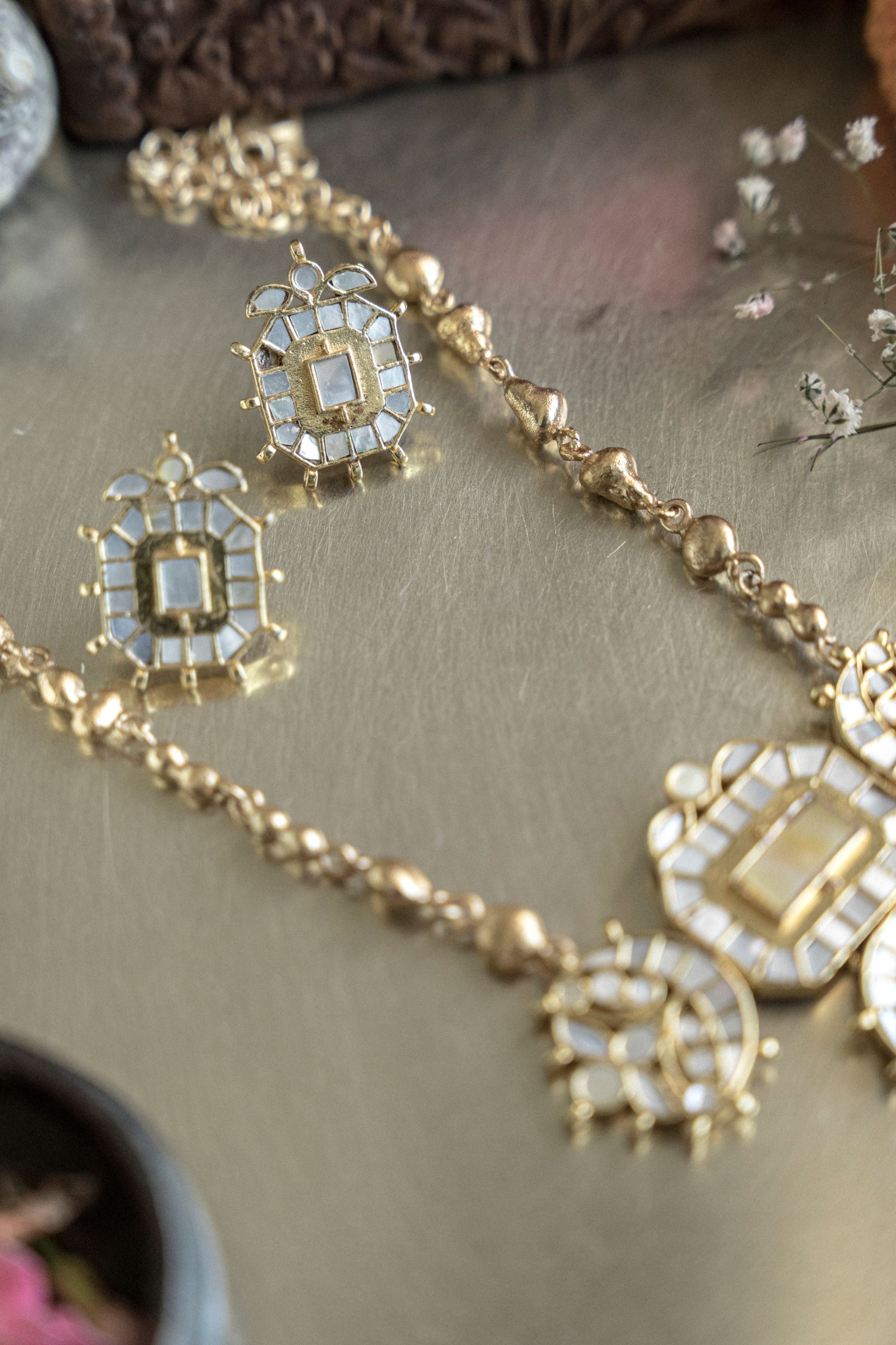 Gold plated Mother of Pearl moon stud necklace set with traditional Kundan detailing on a textured background
