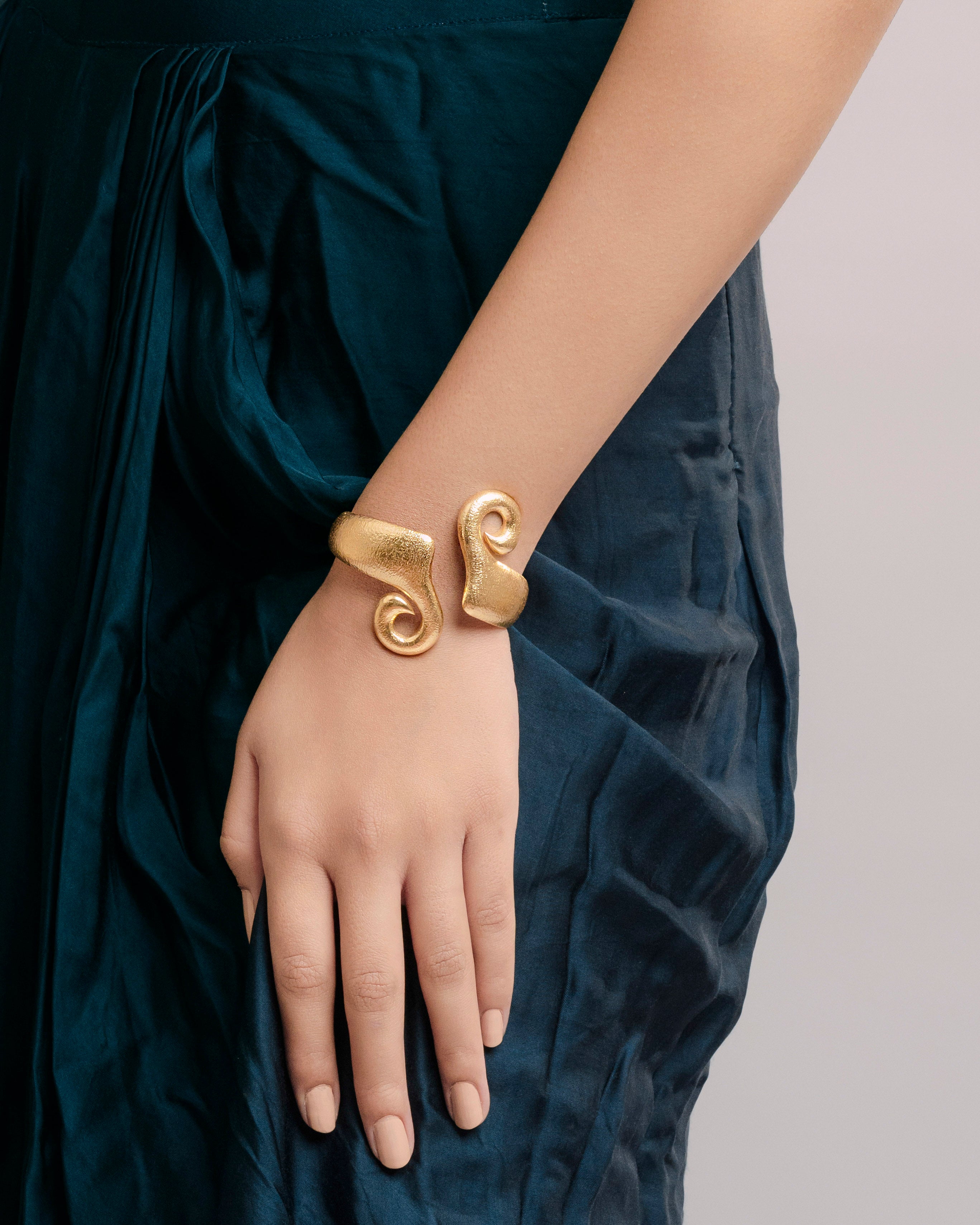 Close-up of an adjustable gold-plated brass statement bracelet featuring a unique hammered texture and a bold, fluid spiral silhouette.