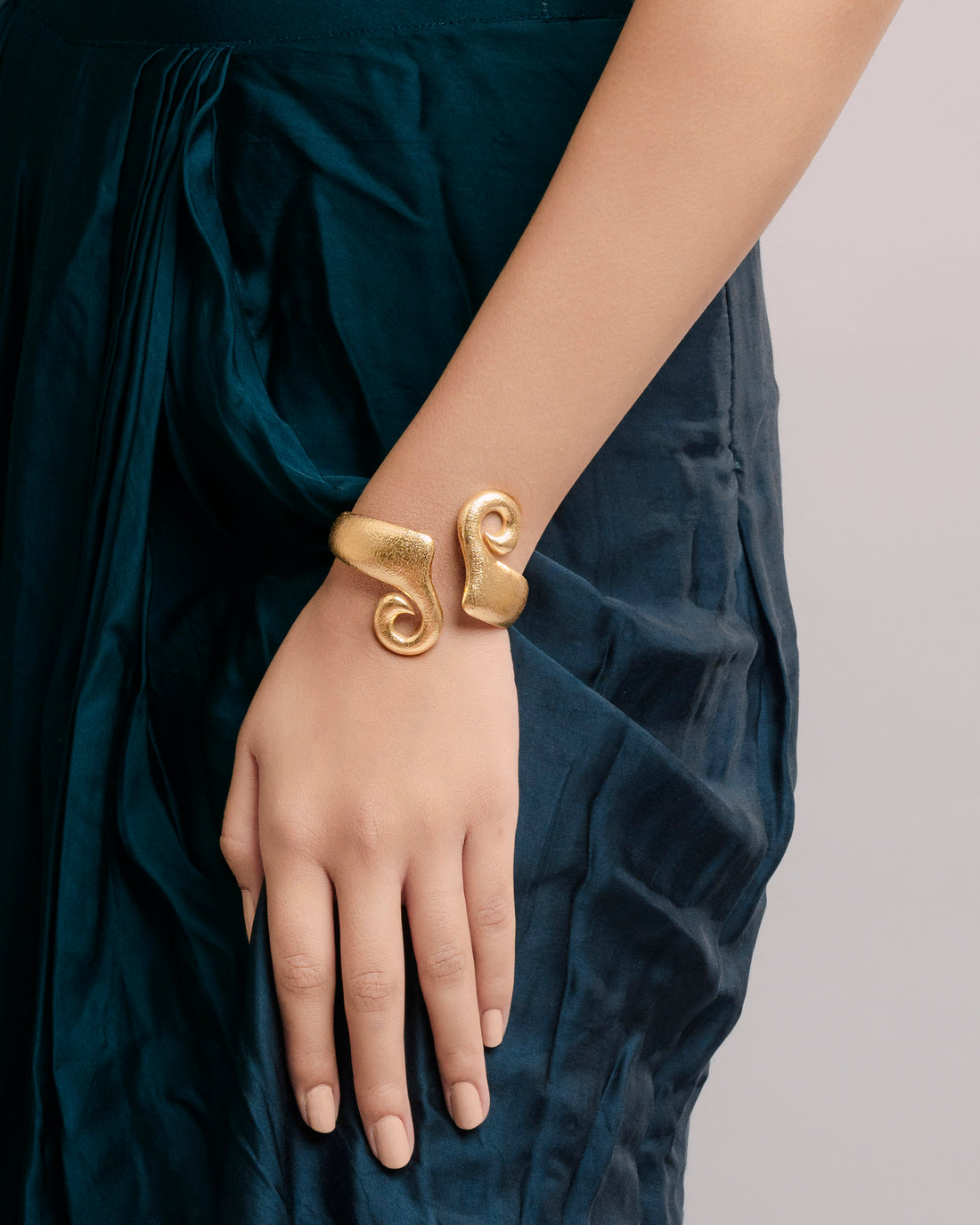 Close-up of an adjustable gold-plated brass statement bracelet featuring a unique hammered texture and a bold, fluid spiral silhouette.