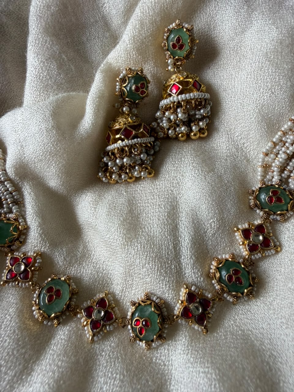 High-quality imitation gold-plated Indian choker necklace decorated with Kundan stones, green enamel, and tiny white pearls alongside matching earrings.