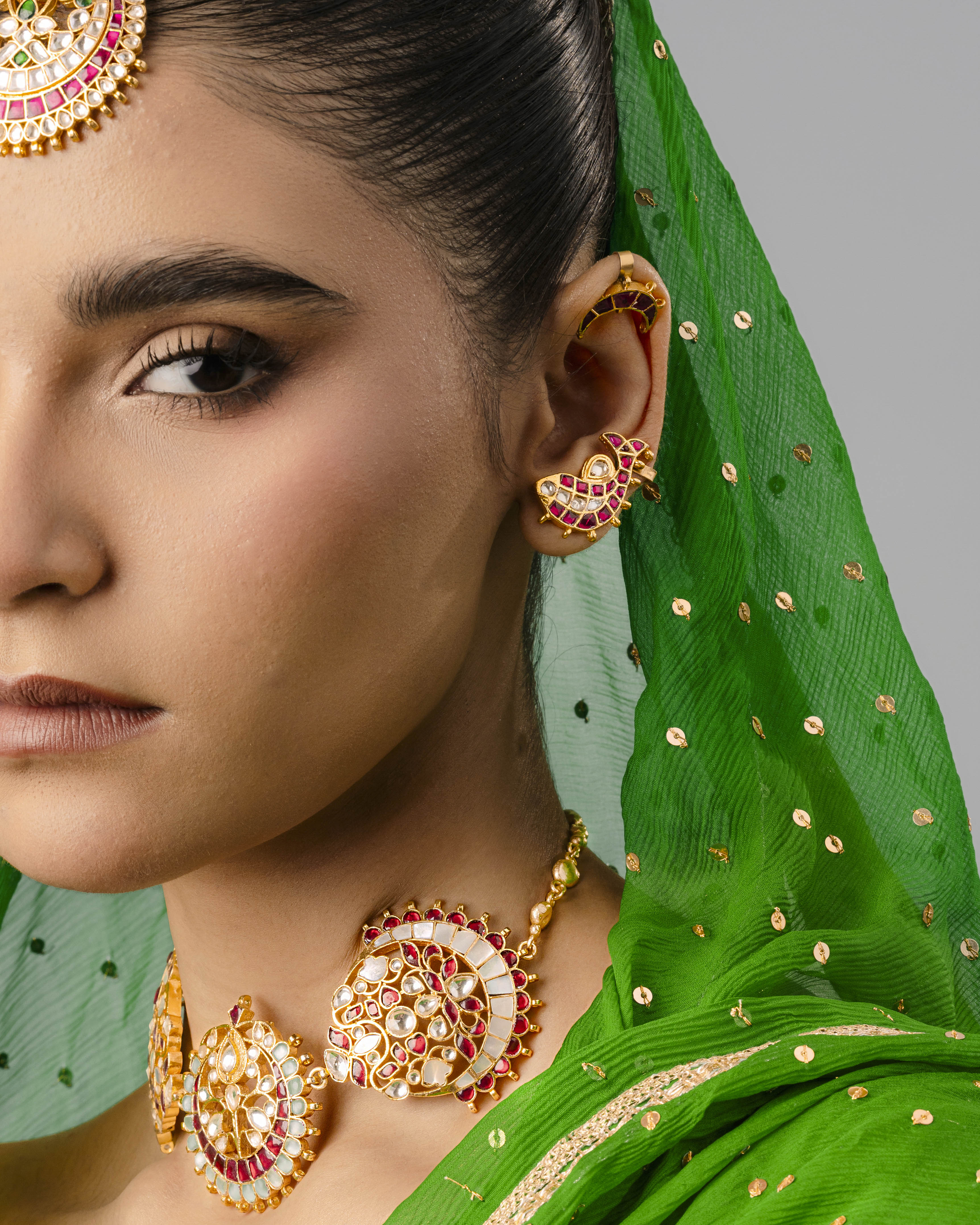 A detailed view of an ornate, gold-plated fish ear cuff on a woman’s ear, matching a traditional Kundan choker and maang tikka.