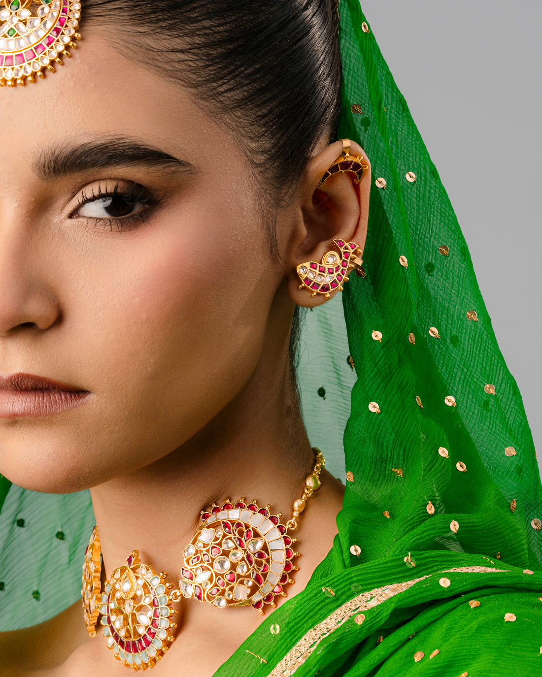 A detailed view of an ornate, gold-plated fish ear cuff on a woman’s ear, matching a traditional Kundan choker and maang tikka.