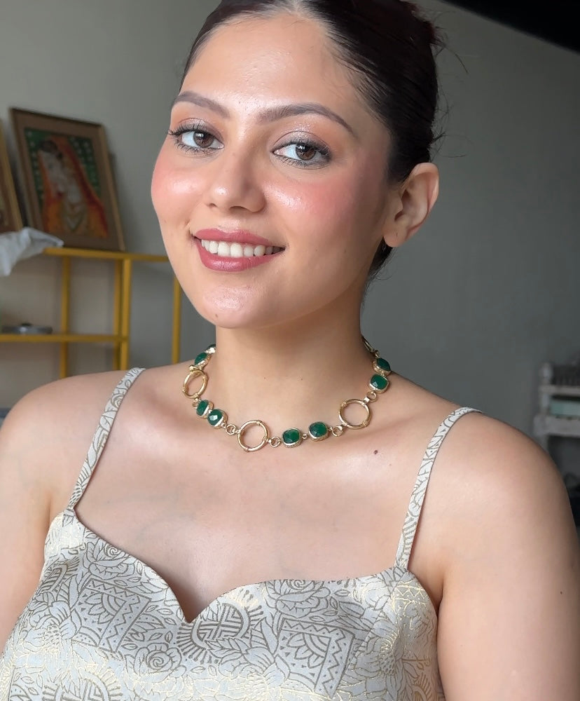 model wearing a gold-plated link necklace accented with vibrant green stones.