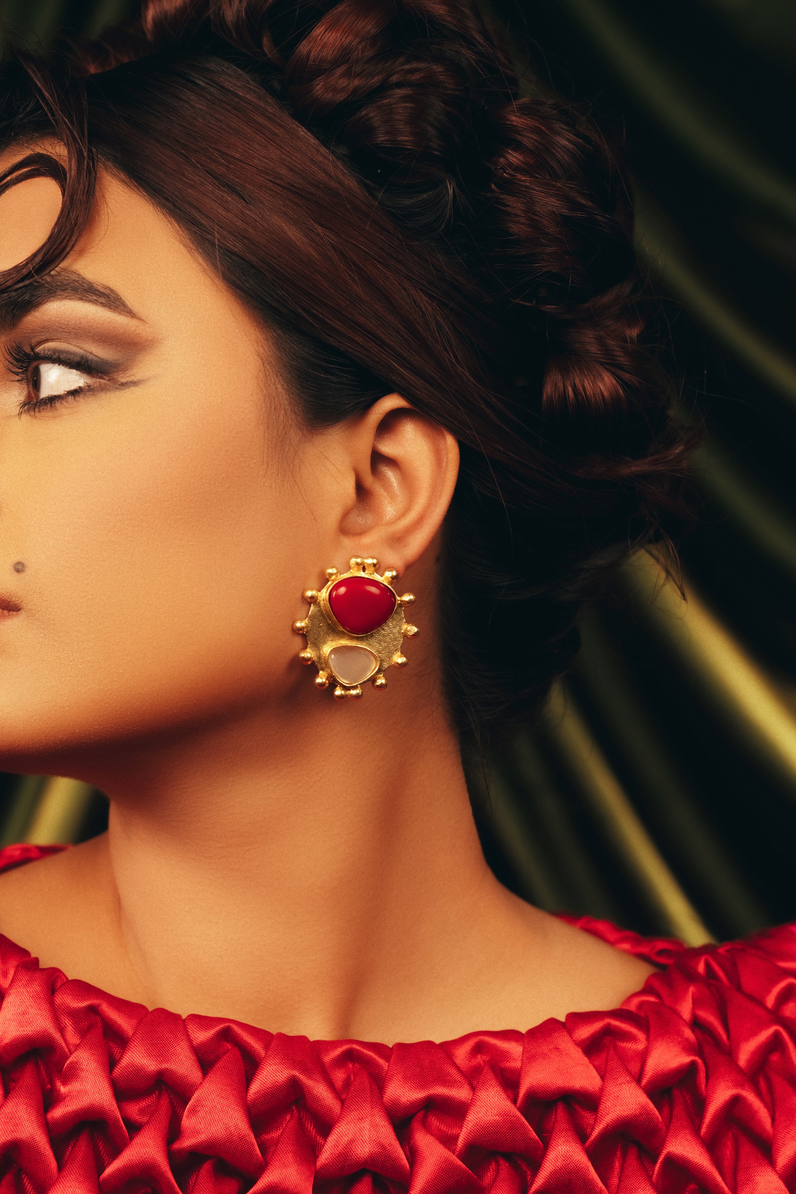 Scarlet Bloom gold floral stud earrings featuring a bold red centre stone and textured gold petals paired with a red outfit.