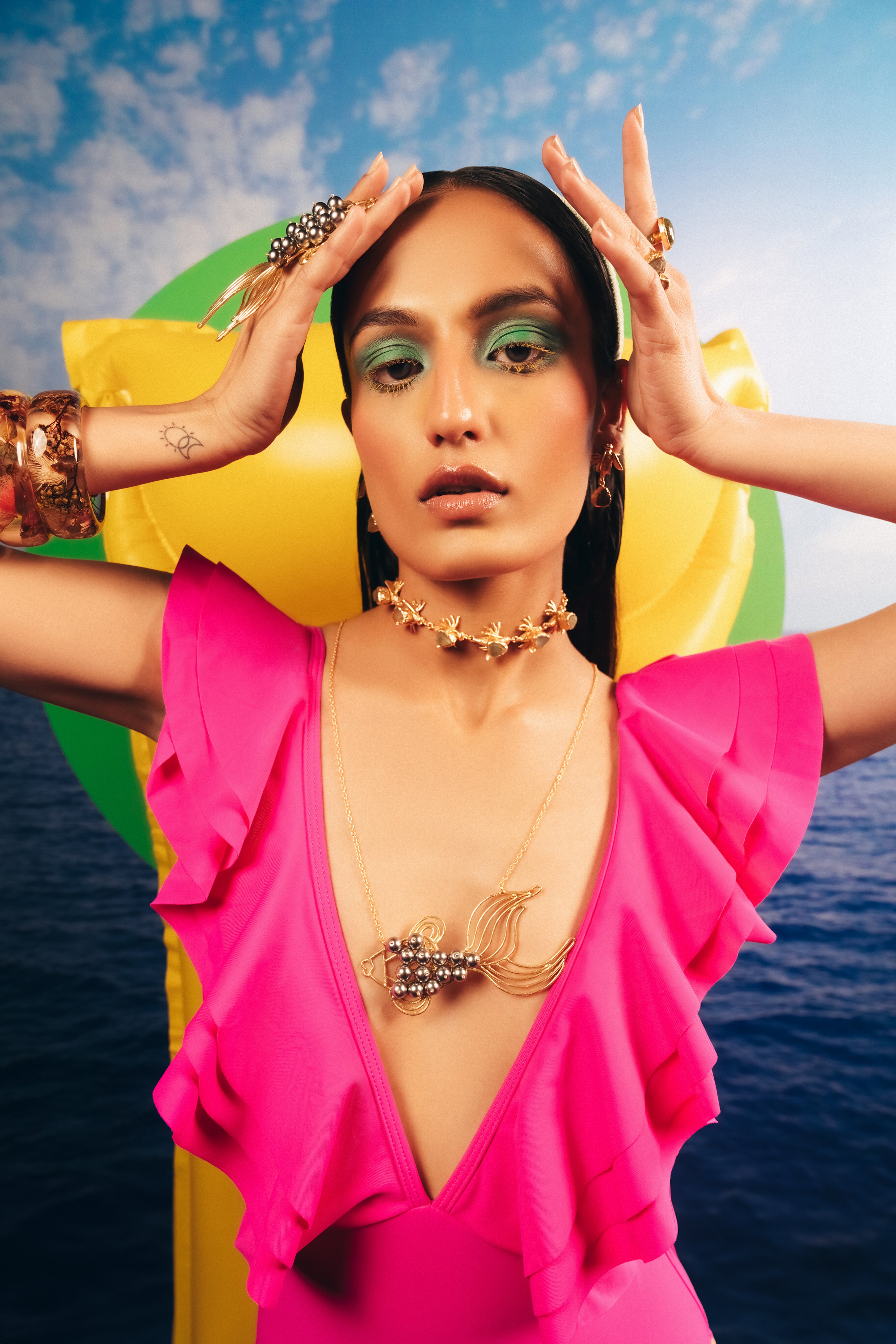Bohemian style gold fish necklace with dark pearl body, styled on natural concrete and stone elements.