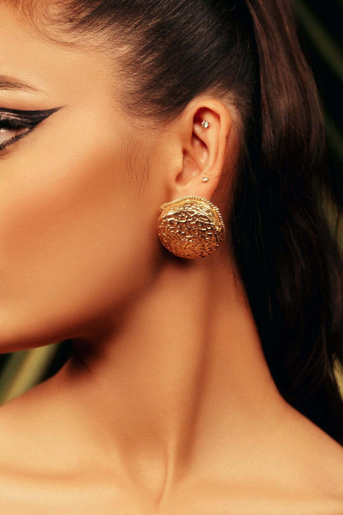 Side view of large circular gold stud earrings worn by a model in black attire.