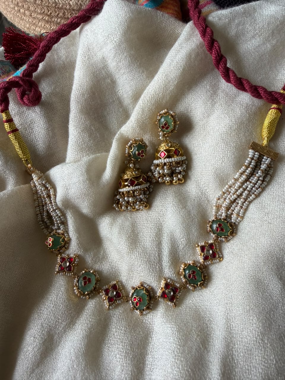 ethnic Indian jewelry set showing an adjustable pearl strand choker with red and green floral Meenakari work and classic pearl-fringe Jhumka earrings.
