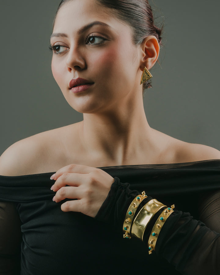 Woman wearing a set of 3 gold-plated stackable kada bracelets with turquoise stones, metallic spikes, and a wavy cuff design by Baala Jewels.