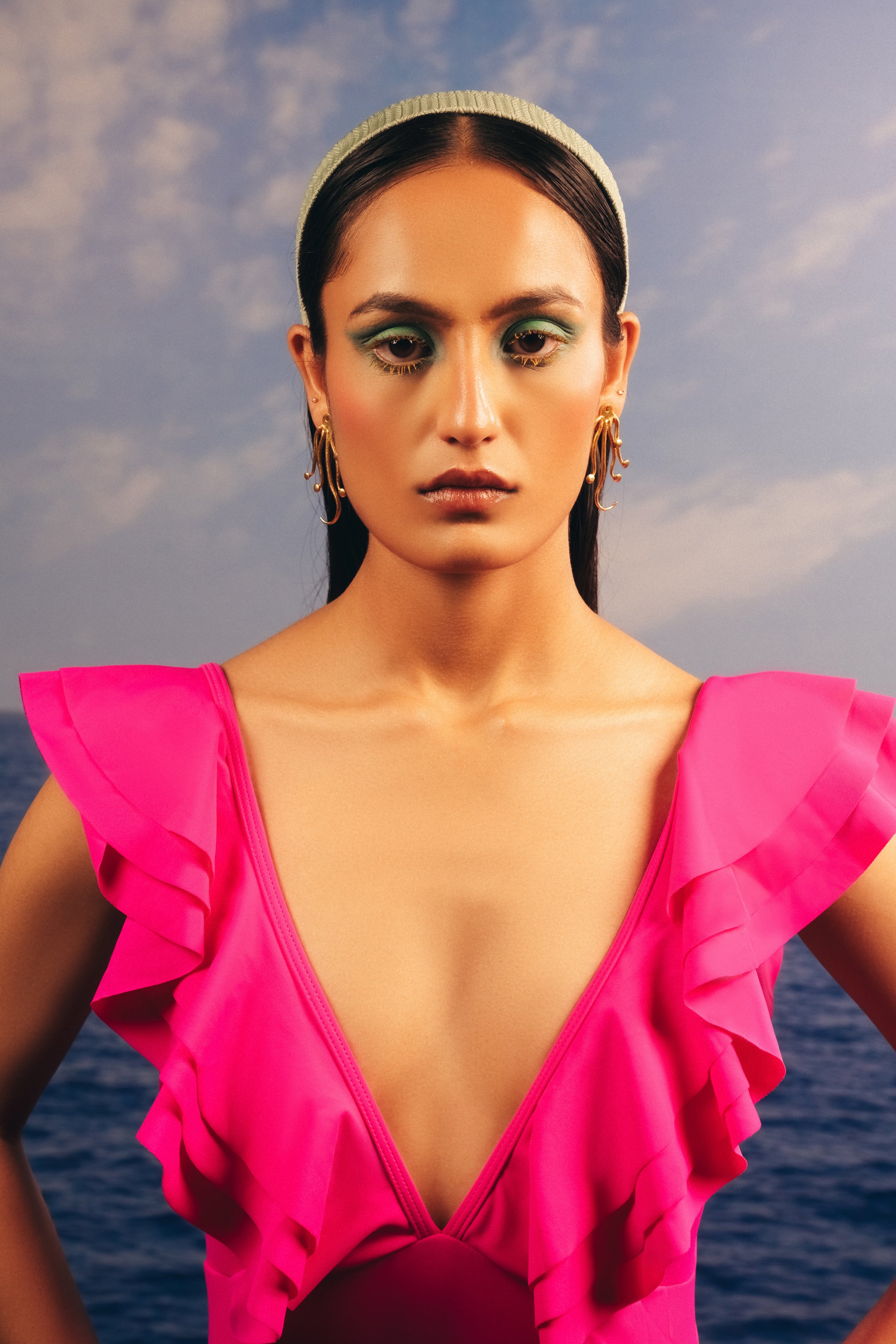 Beach-inspired octopus statement earrings and gold bangles styled on a model by the sea
