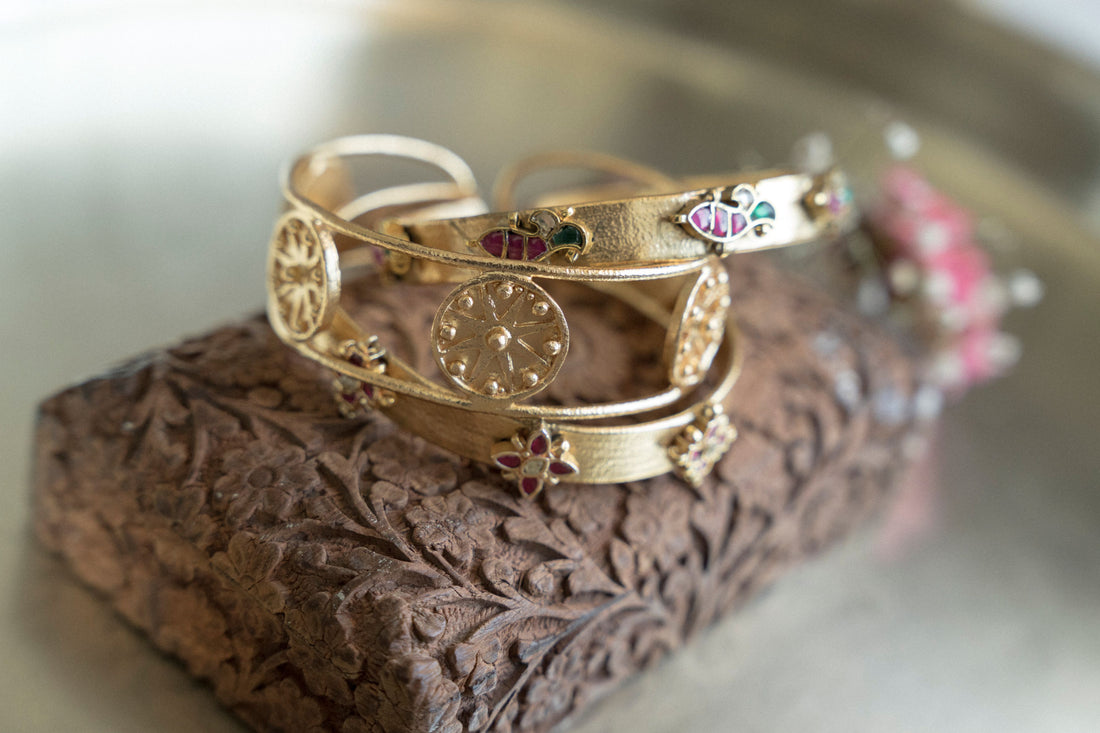 gold stacked bangles featuring circular coin motifs and colorful mother-of-pearl floral accents.