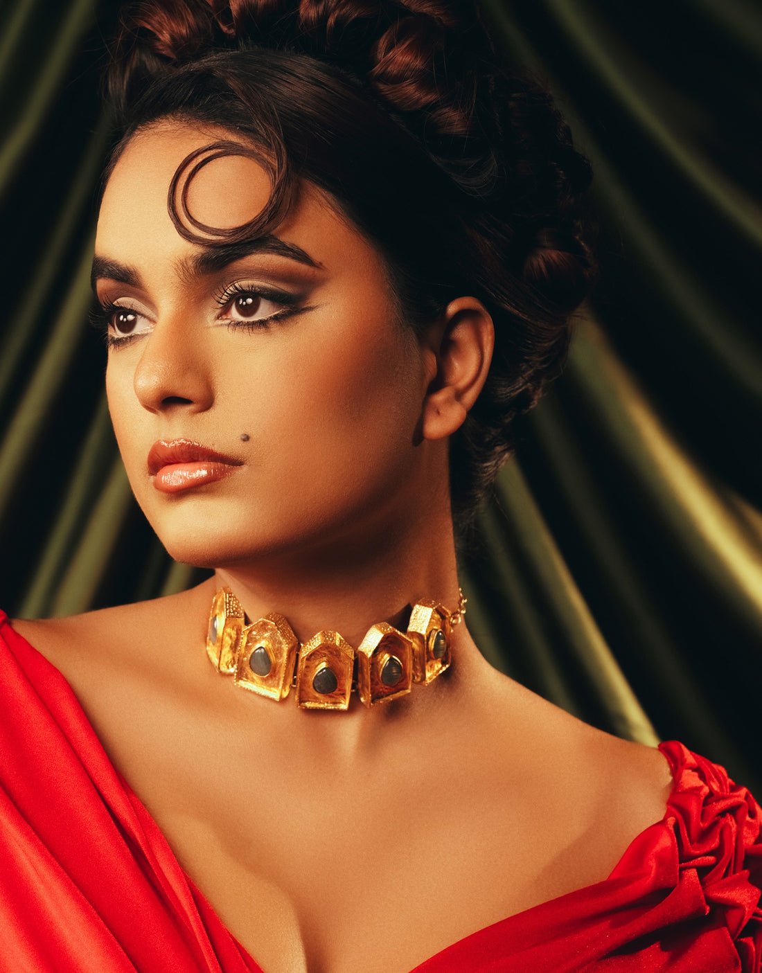 Model wearing the gold Ebon Eclat choker necklace paired with a vibrant red outfit against a textured backdrop.