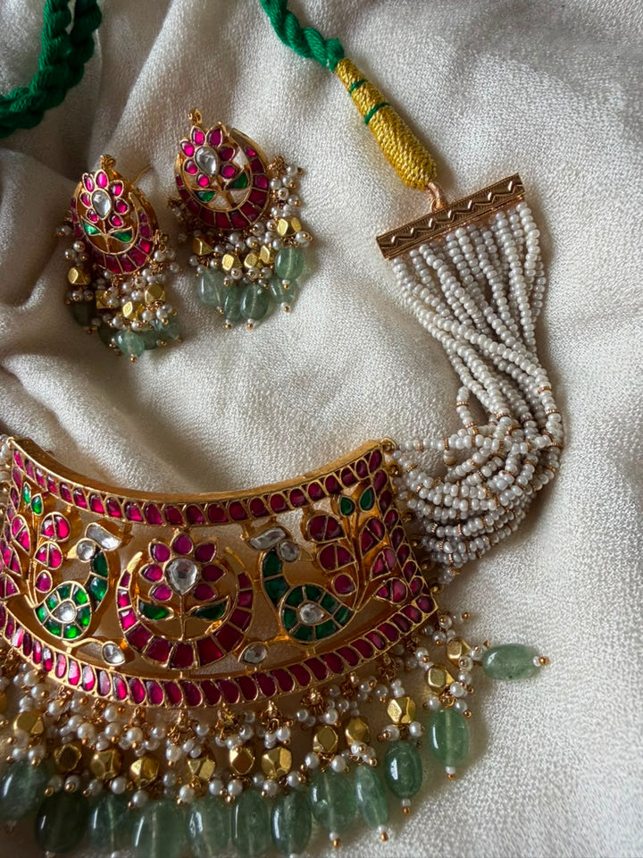 Detailed view of a festive gold-finished choker jewellery set with matching earrings, featuring traditional Meenakari enamel, Kundan embellishments, a woven pearl strap, and green bead droplets.
